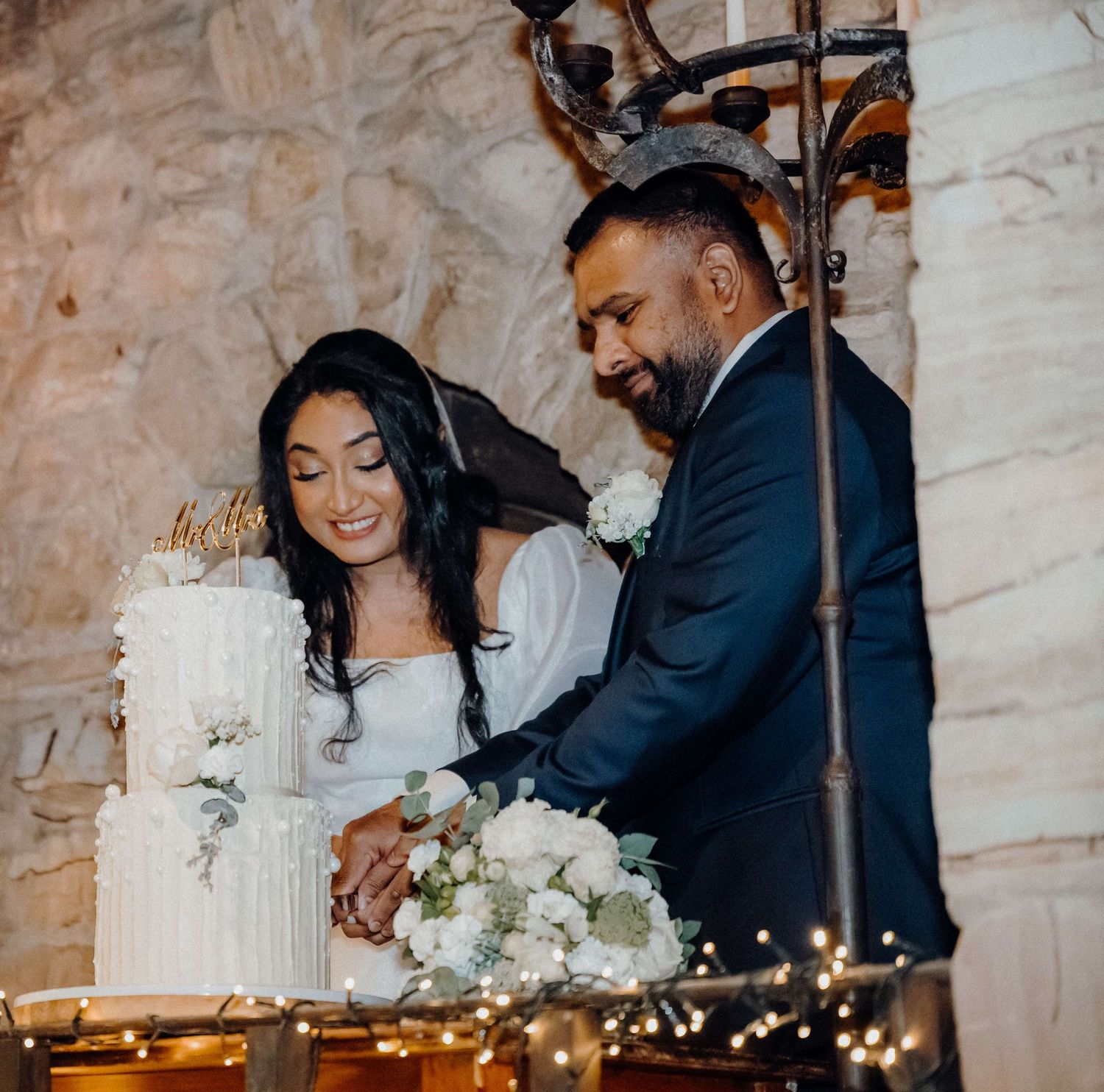 A wedding couple cutting their elegant white tiered cake together at their reception celebration.
