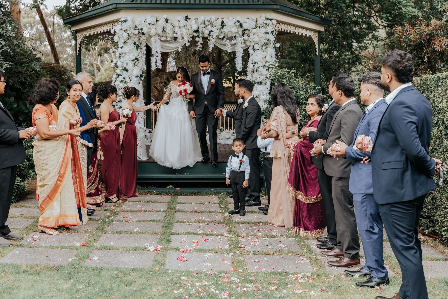 Bridal party and guests line up outside on grass to celebrate newlyweds during outdoor wedding ceremony.
