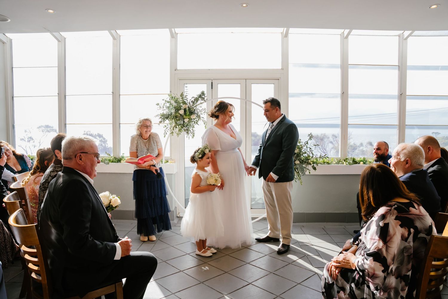 Family and friends celebrate at a bright, modern waterfront wedding ceremony in an airy white venue.