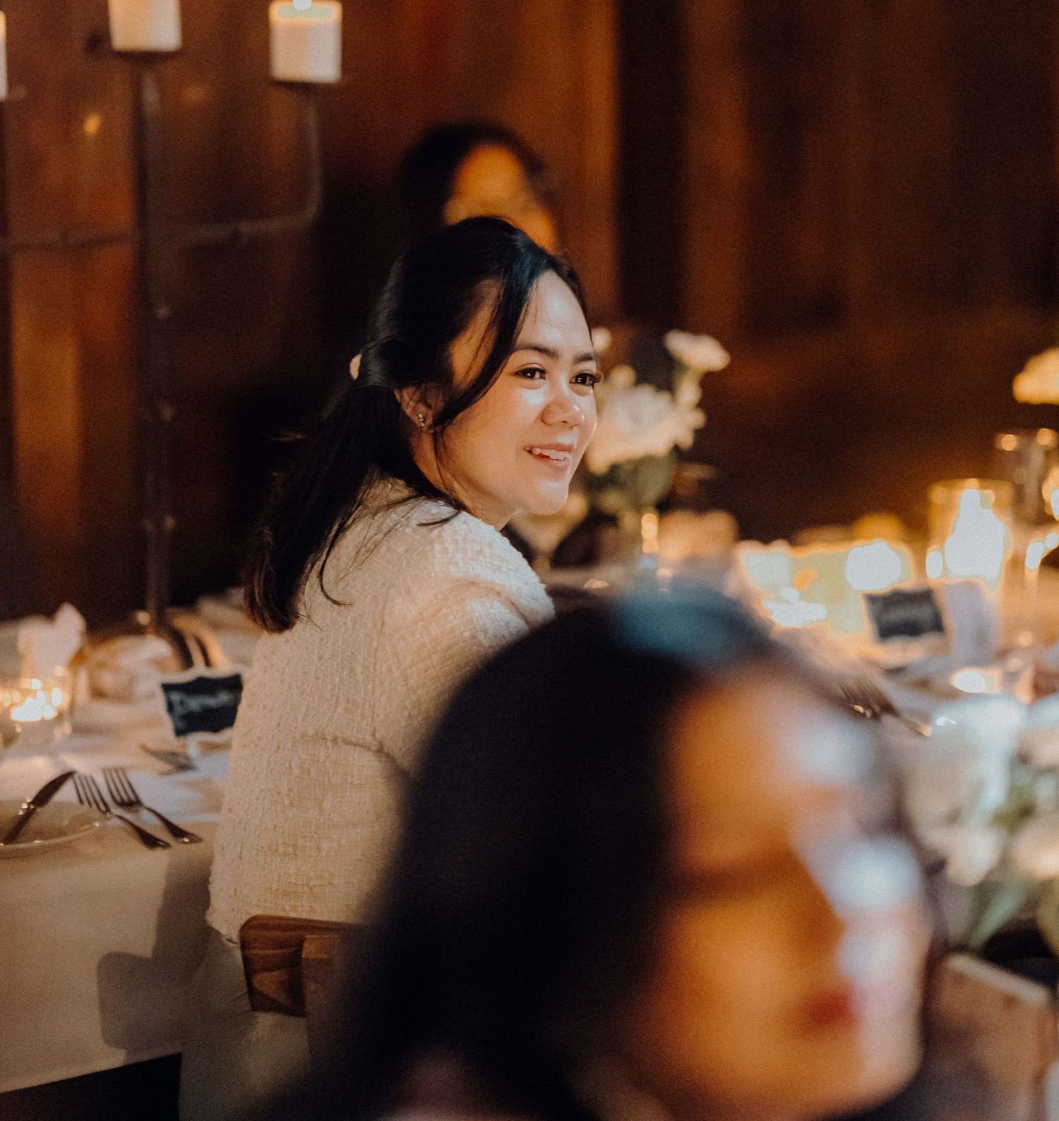Person sitting at an elegant candlelit dinner table with warm ambient lighting in a rustic wooden interior.