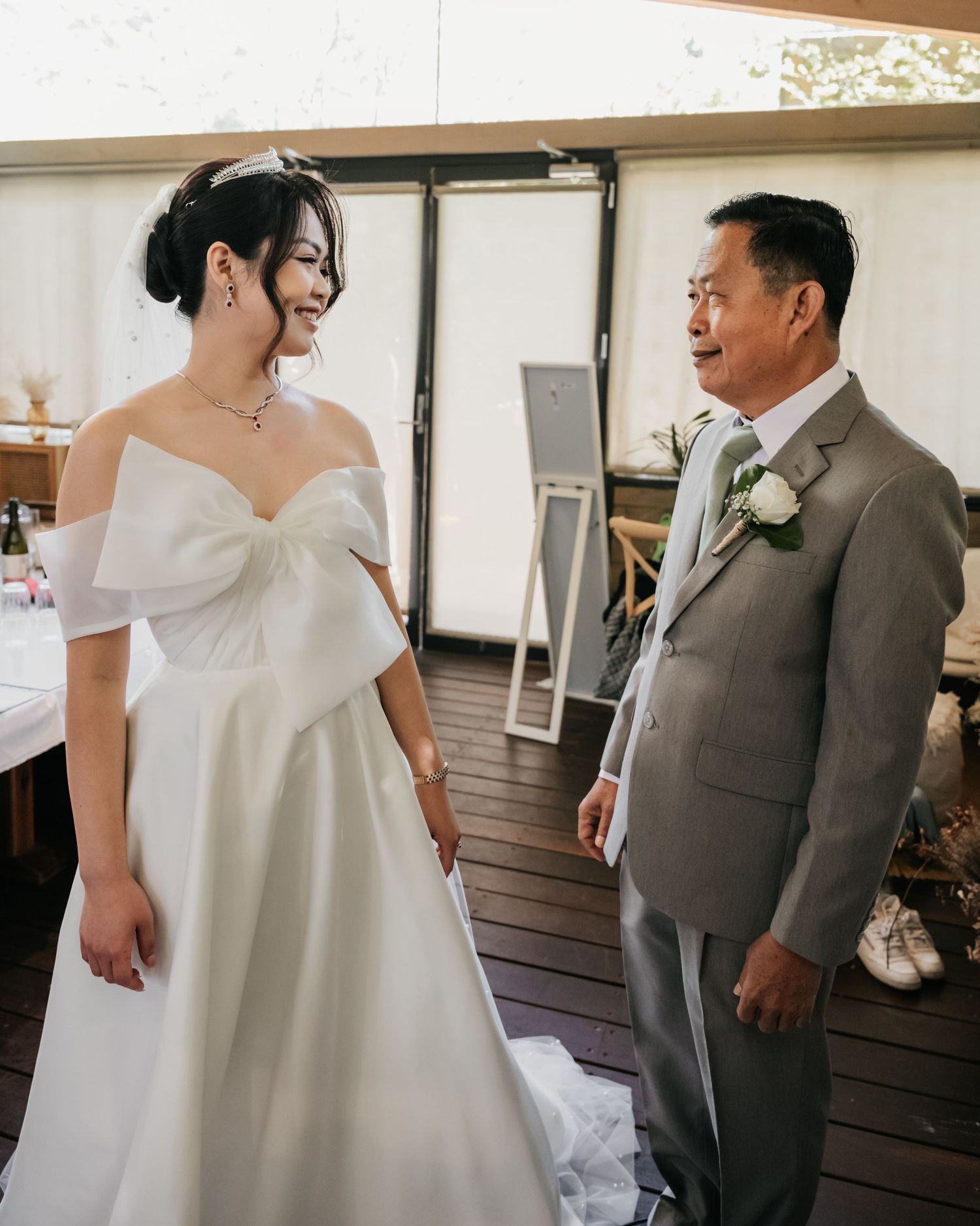 A touching moment between a bride in an elegant off-shoulder white gown and a guest in a grey suit at a wedding venue.