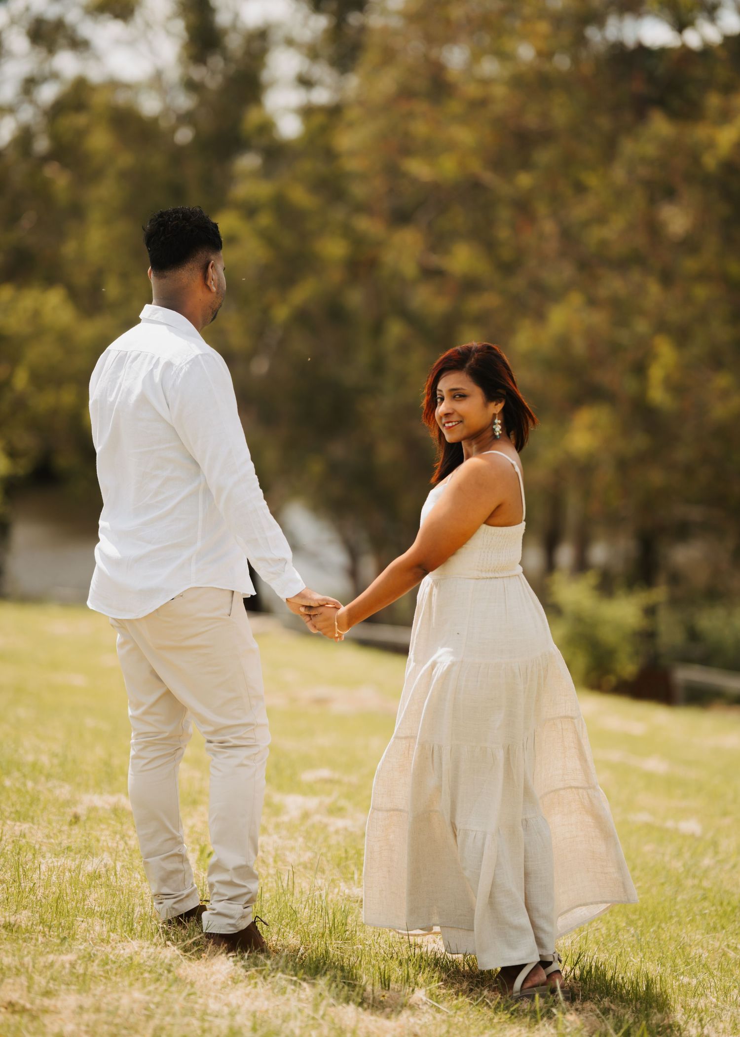 A couple in white outfits sits together on grass during a romantic outdoor photoshoot session.