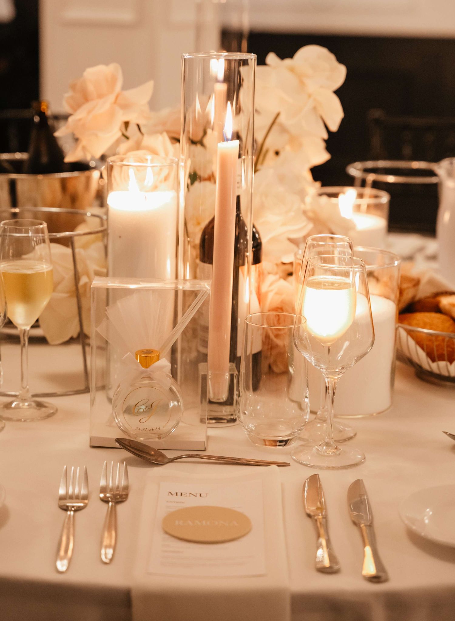 An elegant white tablecloth dinner setting with glowing candles, wine glasses and formal place settings in warm lighting.
