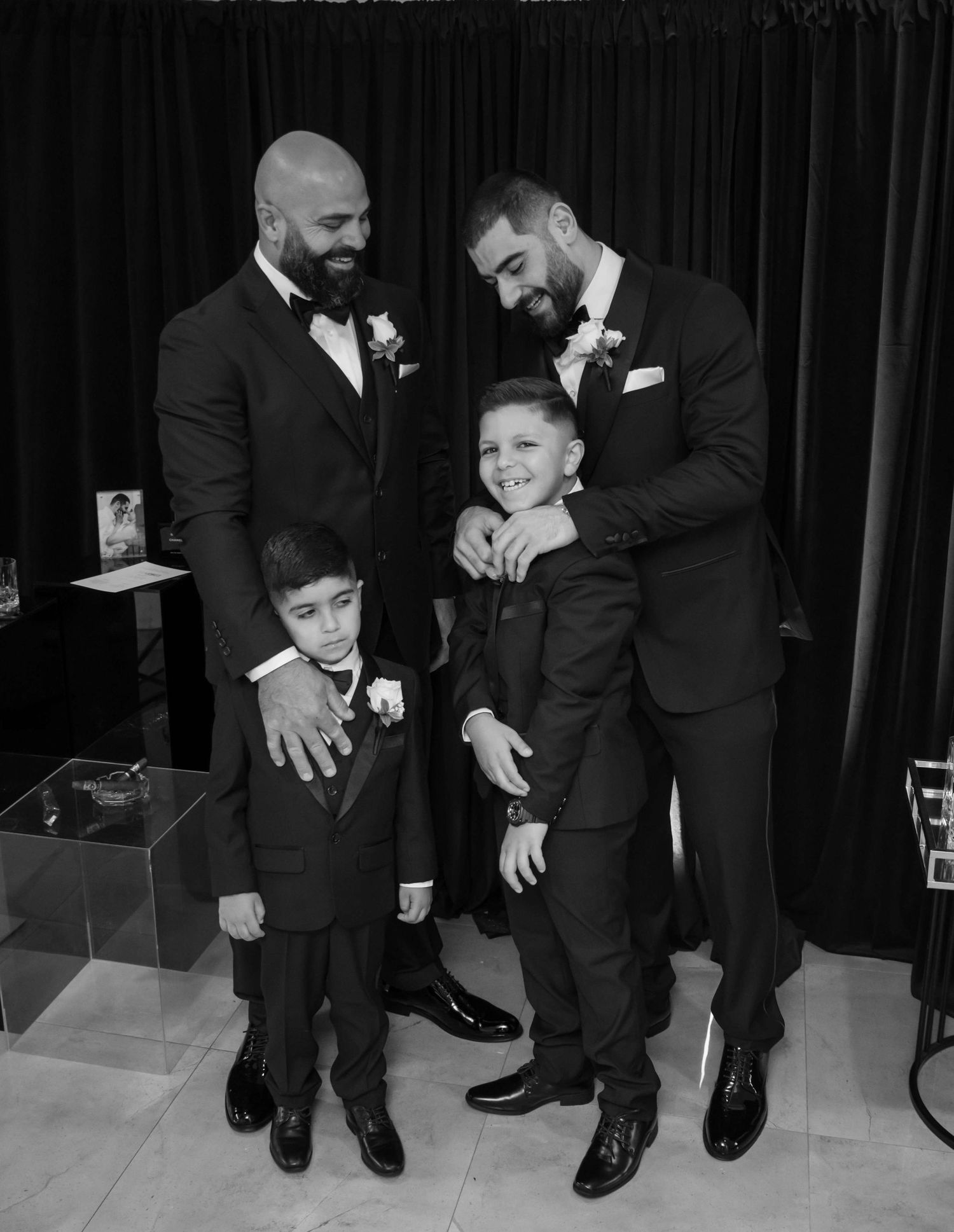 A black and white photo of adults and children in formal attire, wearing matching black suits at an elegant event.
