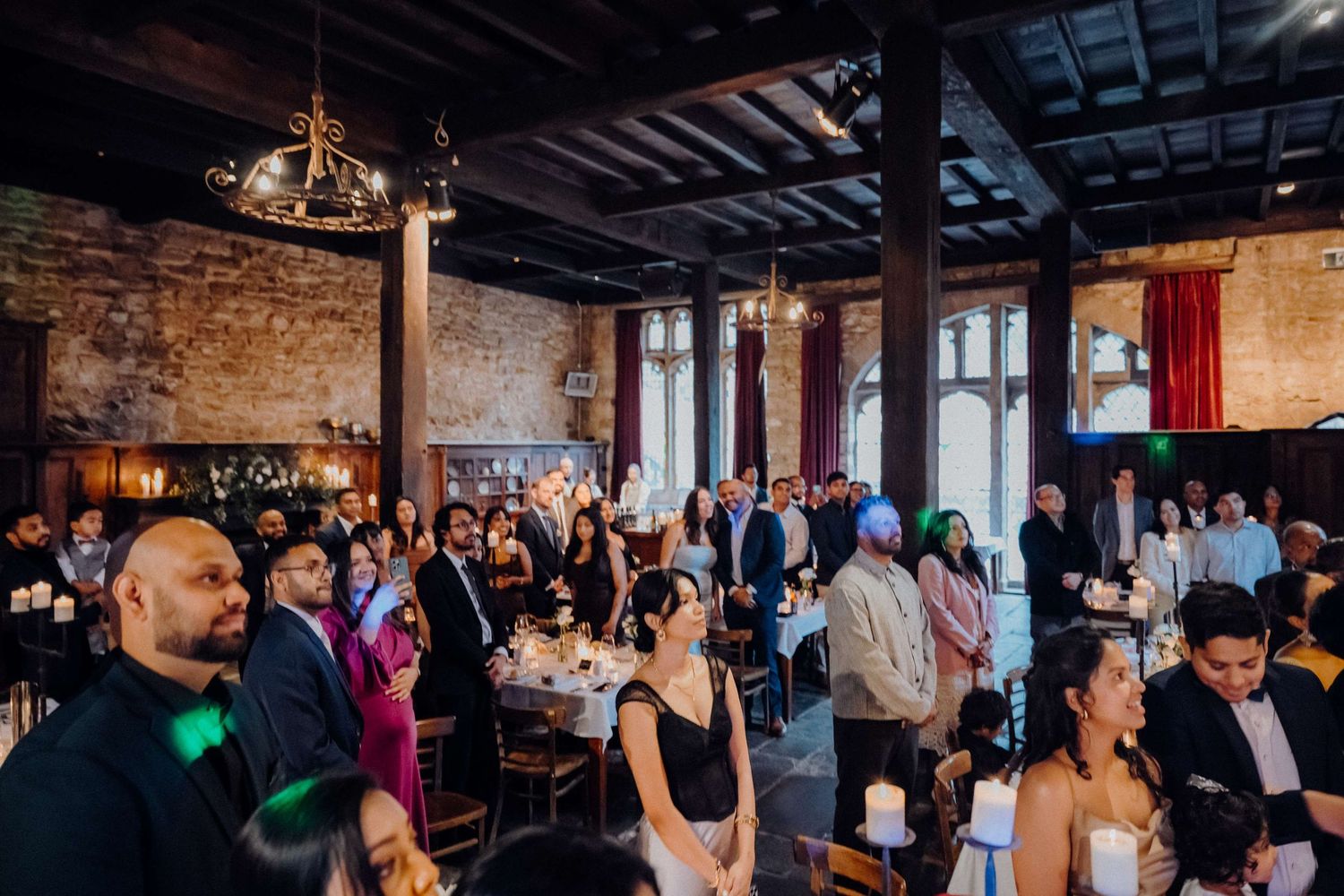 Wedding guests gather in a rustic reception venue with exposed brick walls and wood beam ceiling.