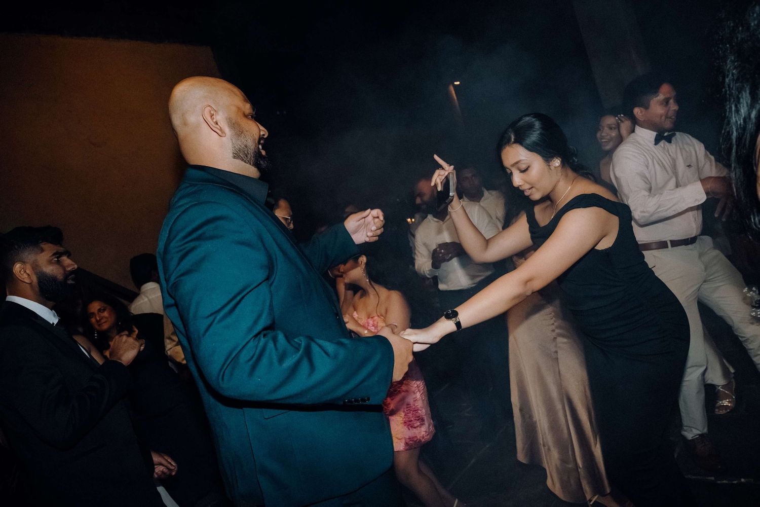 People dancing together in formal attire at an evening social event in a dimly lit room.