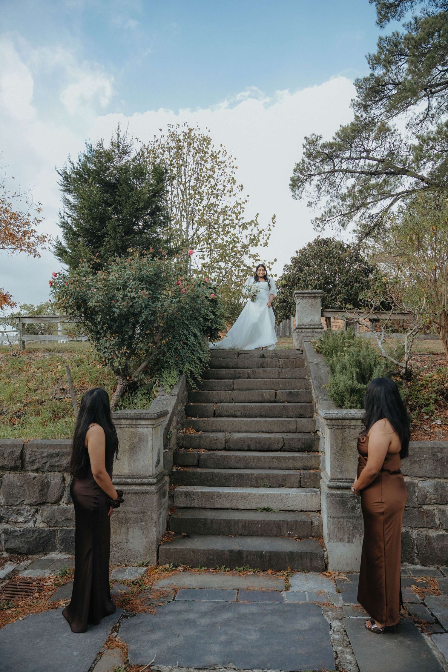 People standing at the base of stone stairs during an autumn wedding ceremony in an outdoor garden setting.