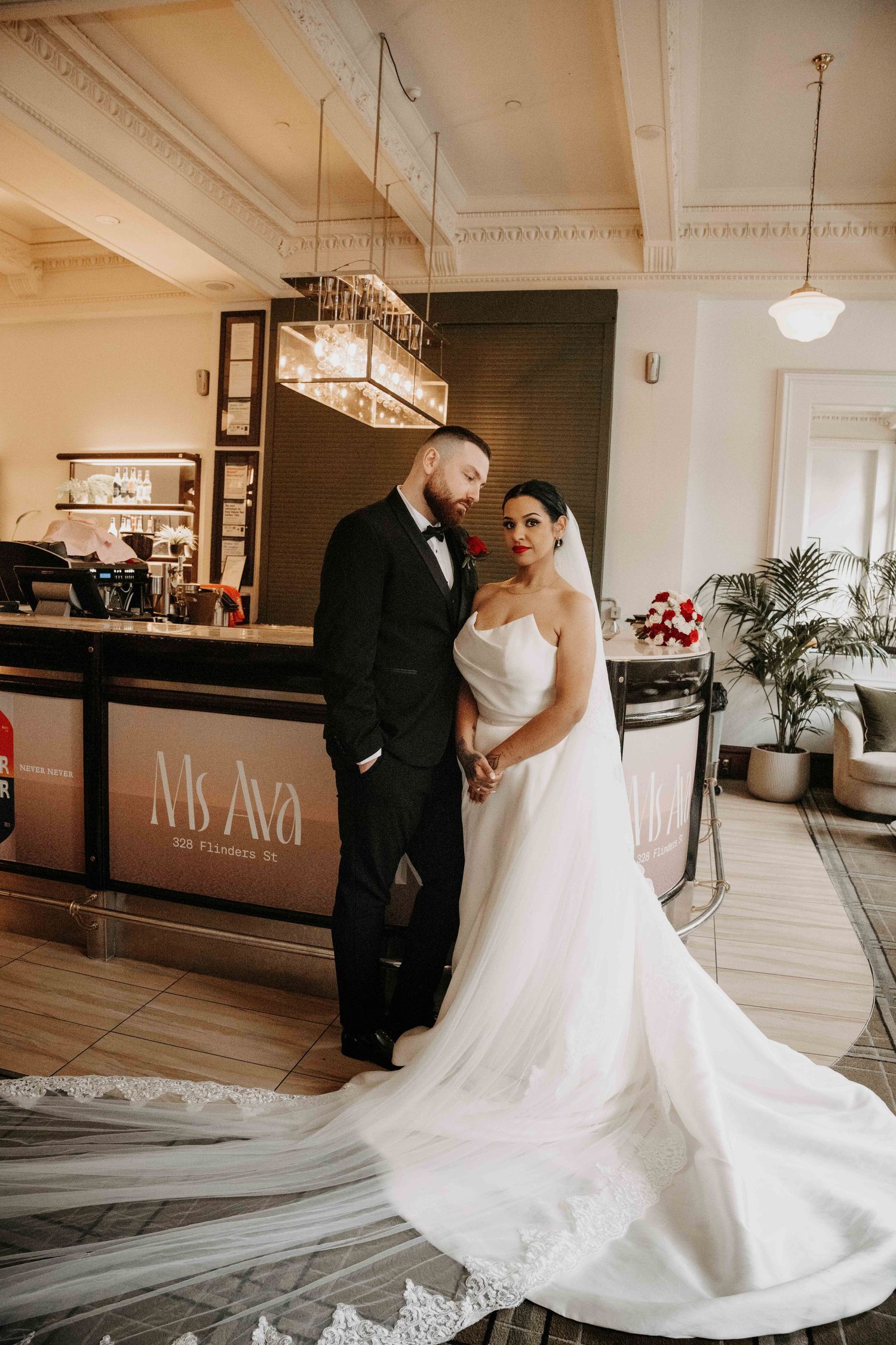 Bride in strapless white gown and groom in black tuxedo pose together inside elegant Ms Ava venue on wedding day.