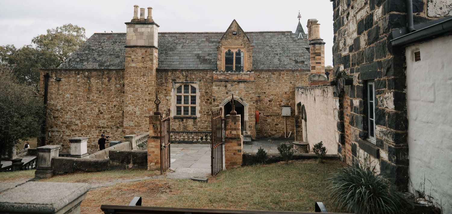 Historic stone cottage with arched entryway and dormers set against a moody sky in a Scottish countryside setting.