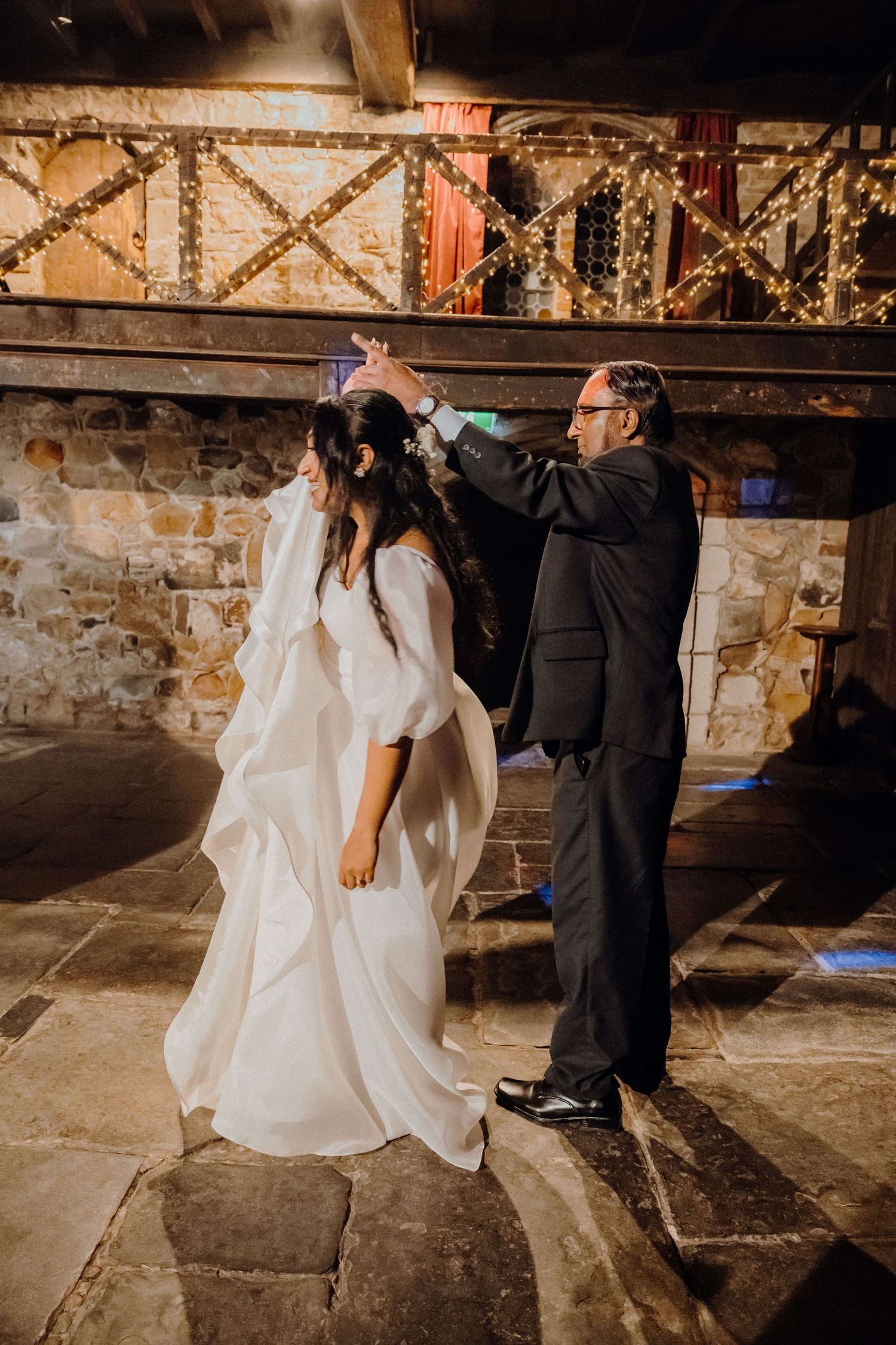 A bride and groom perform an intimate dance sequence in a dimly lit rustic stone cellar venue.