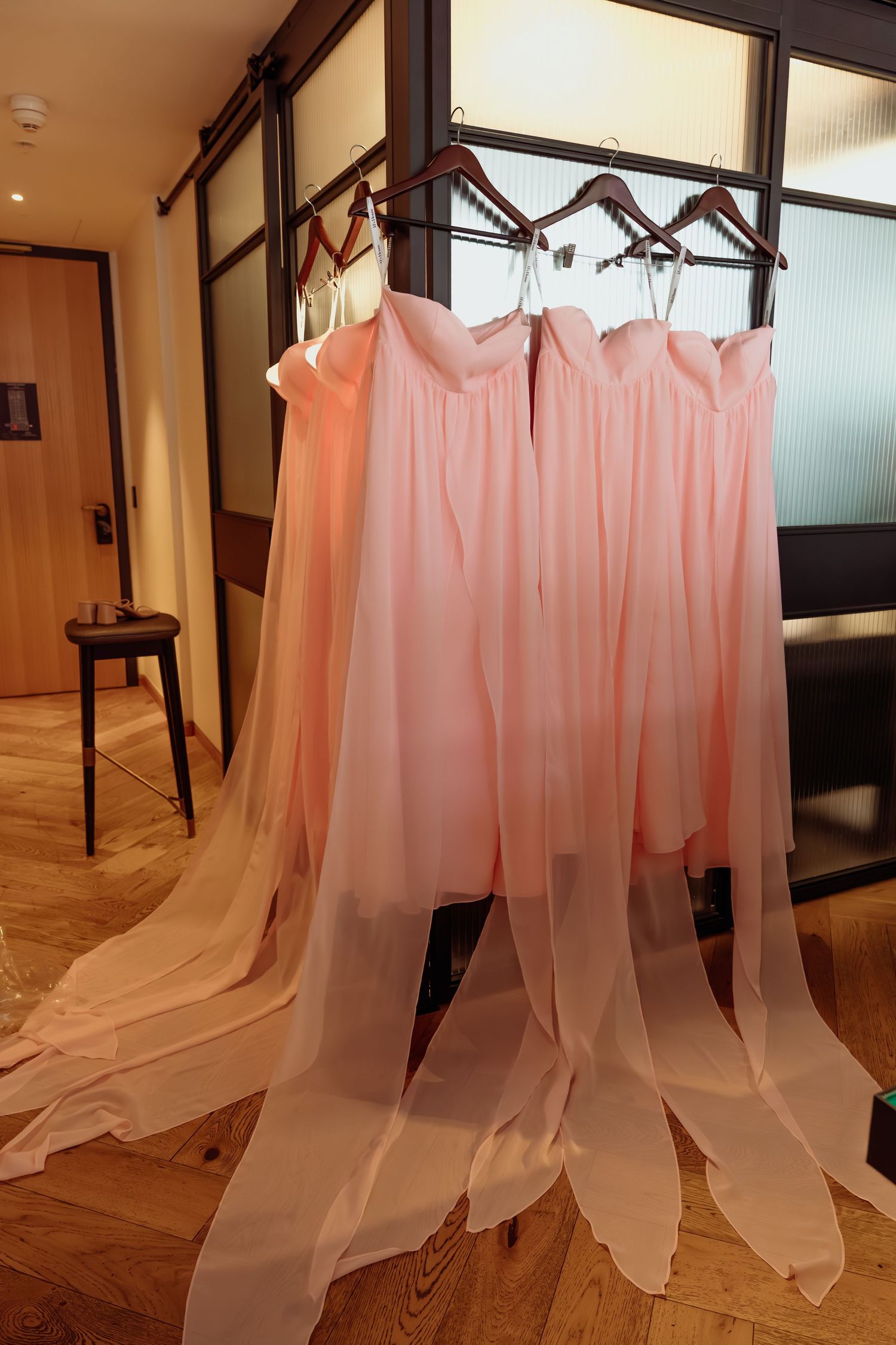 Multiple sheer pink curtains or fabric panels hanging from wooden hangers in an interior space with hardwood floors.