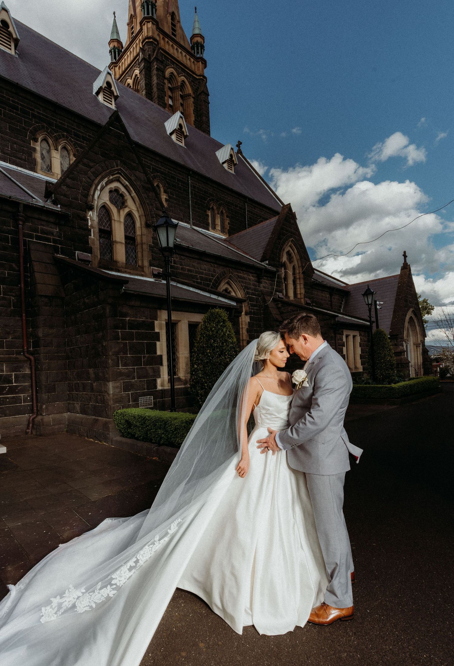 A romantic wedding moment captured outside a gothic stone church with dramatic architecture and flowing white dress.