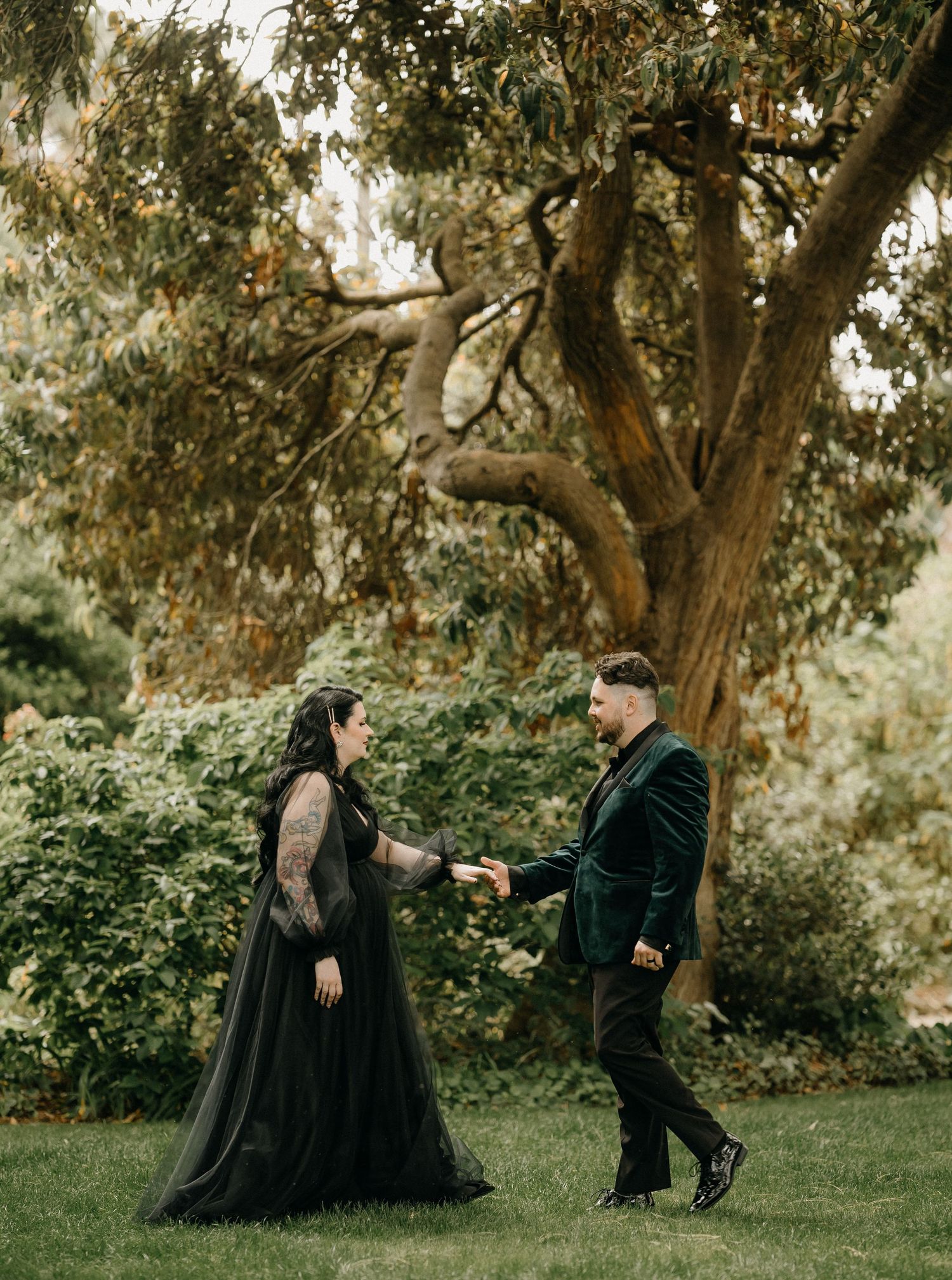 A couple in dark formal attire shares romantic moments in a series of artistic photos under large trees in a garden setting.