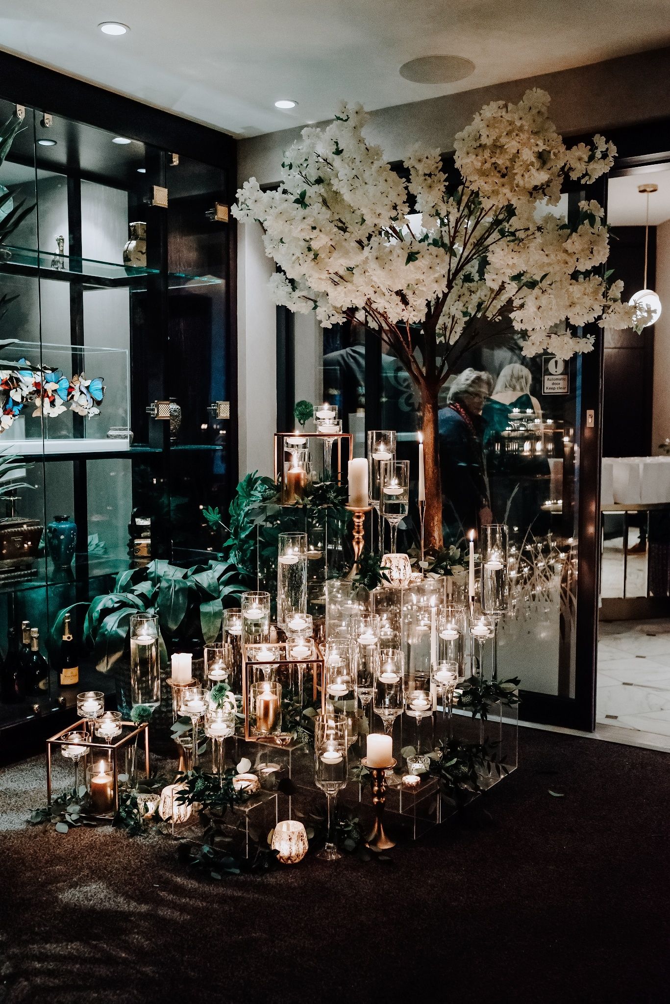 Elegant indoor wedding reception decor featuring illuminated lanterns and white cherry blossom trees in a modern venue.