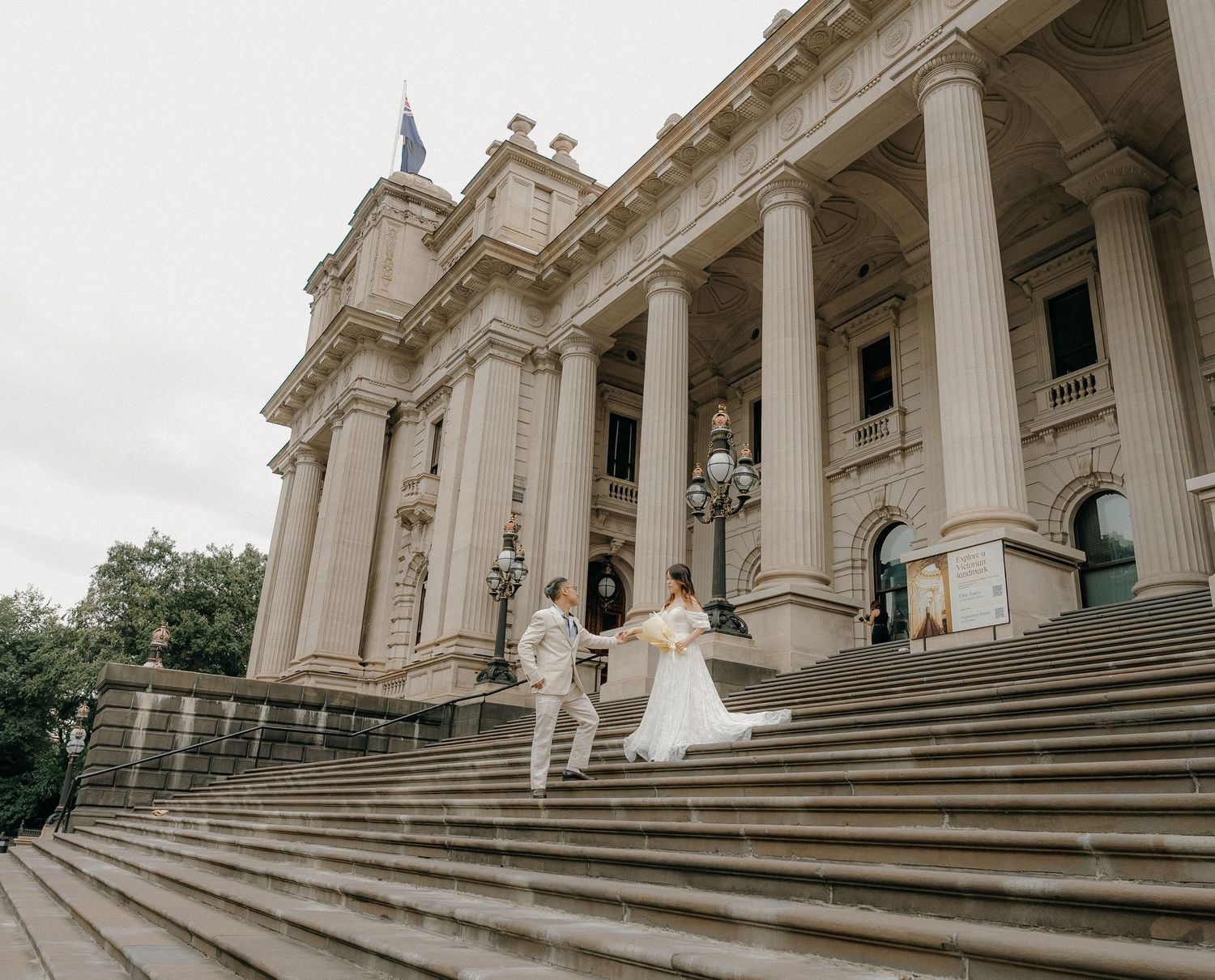 Elegant couple celebrates on grand stone steps of historic Parliament House in Melbourne with ornate classical columns.