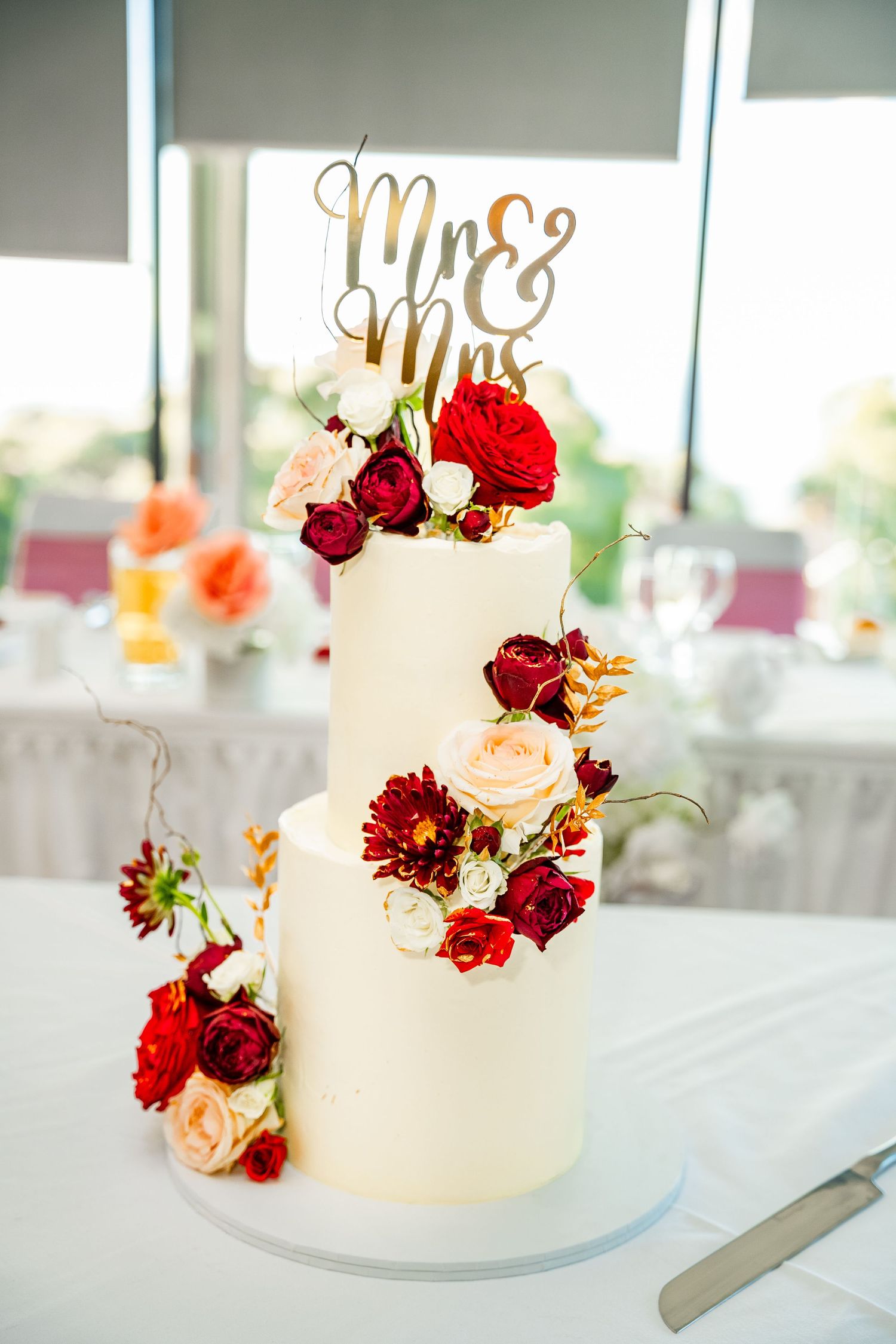 Elegant white wedding cake decorated with cascading red and blush roses on a light blue cake stand.