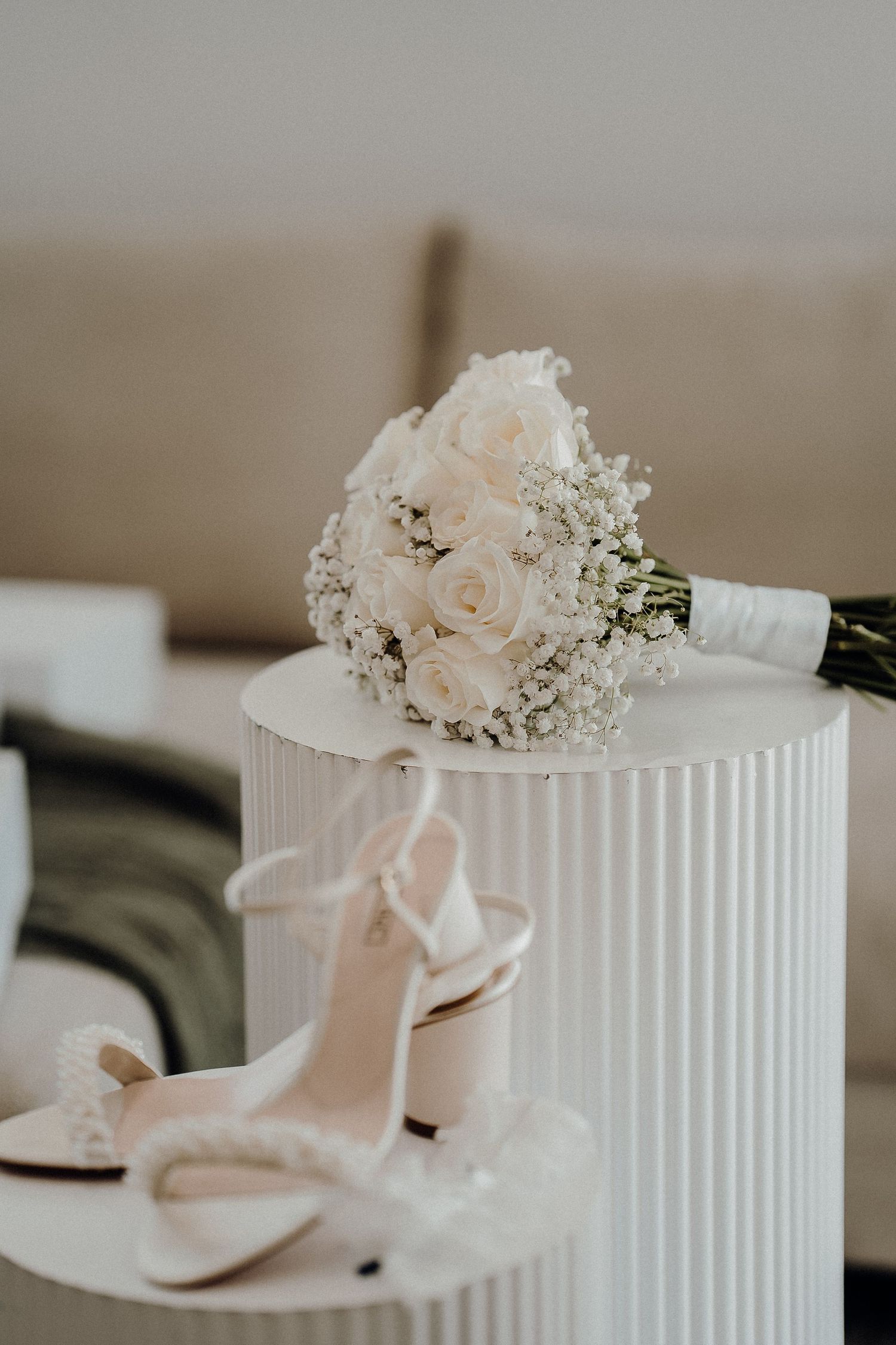 Delicate pink bridal shoes and floral hair accessories displayed on white pedestals with modern pleated design details.