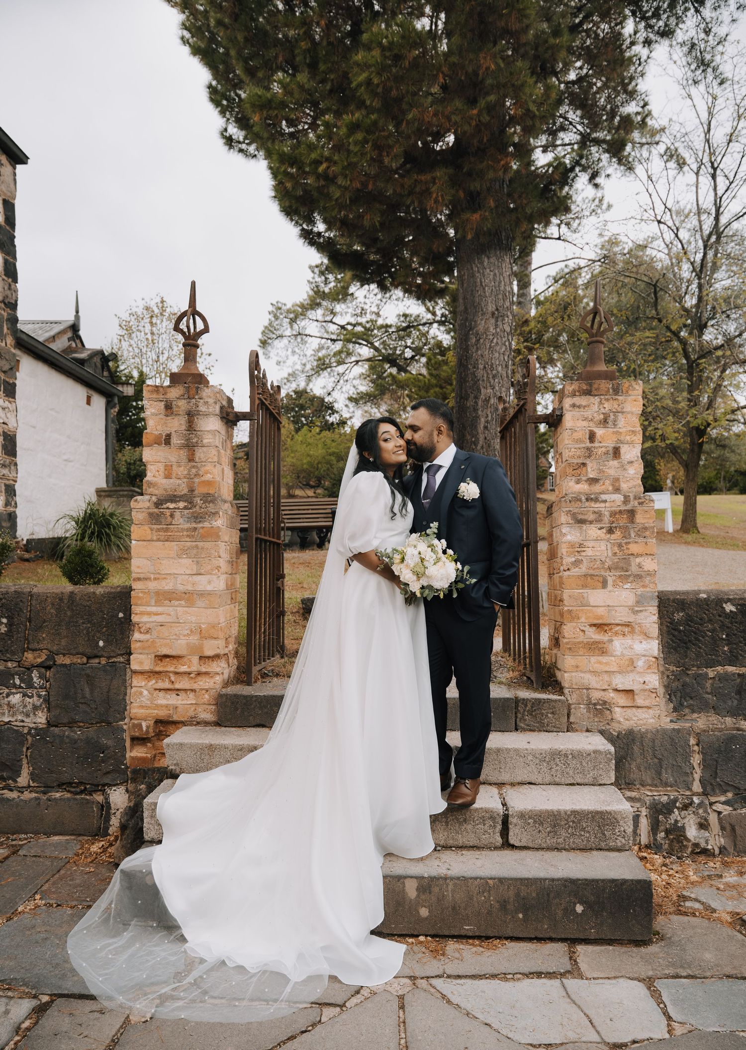 A couple shares an intimate moment on stone steps between brick pillars at a historic church entrance.