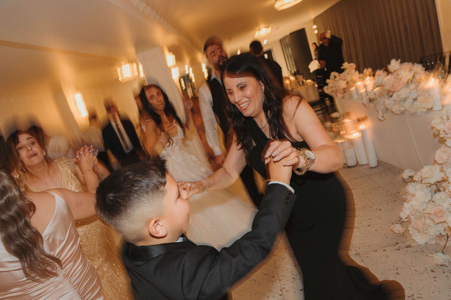 A festive wedding reception scene shows party guests dancing and celebrating on a brightly lit dance floor.
