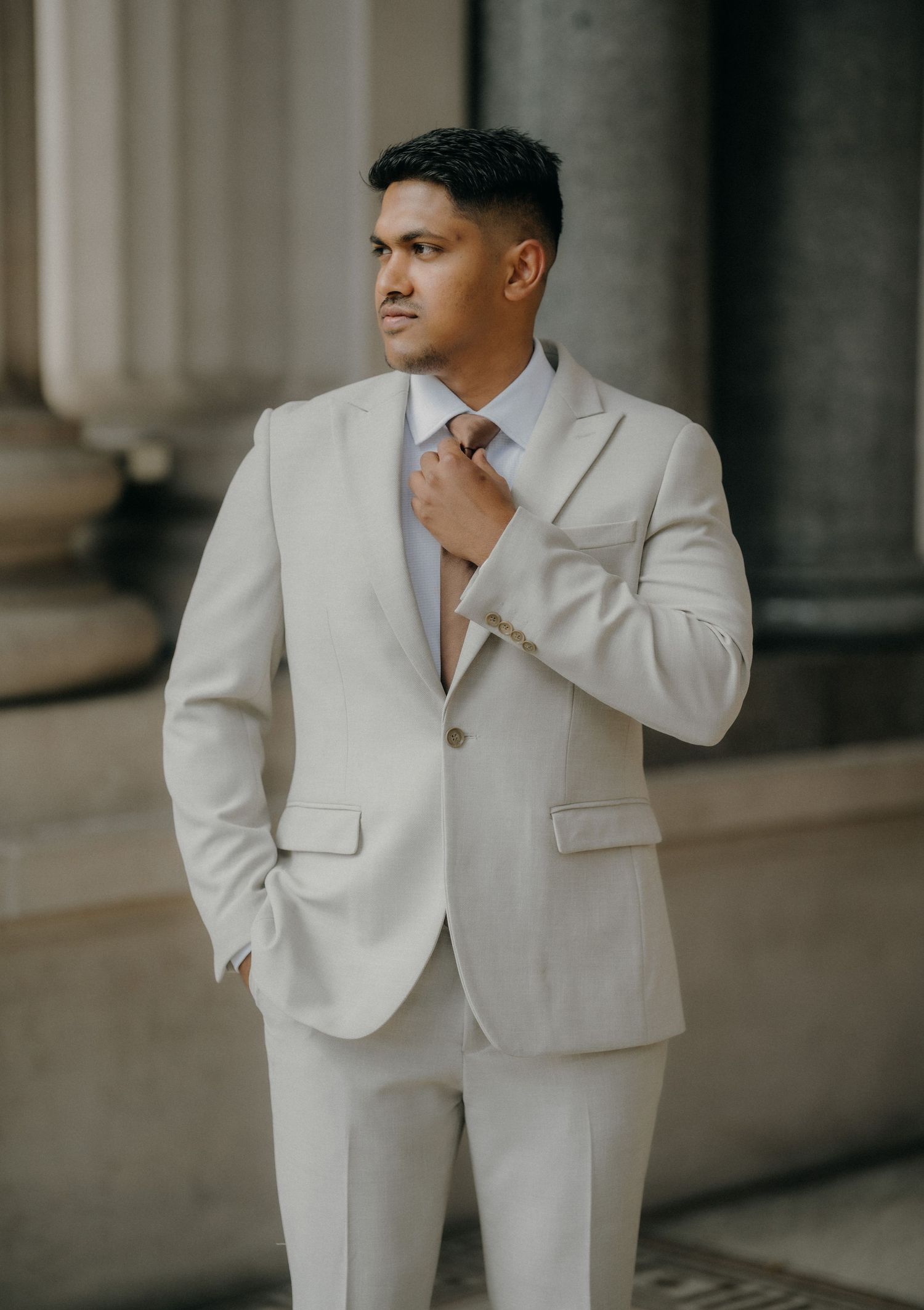 A person poses in an elegant white suit against a neutral backdrop in a series of fashion portraits.