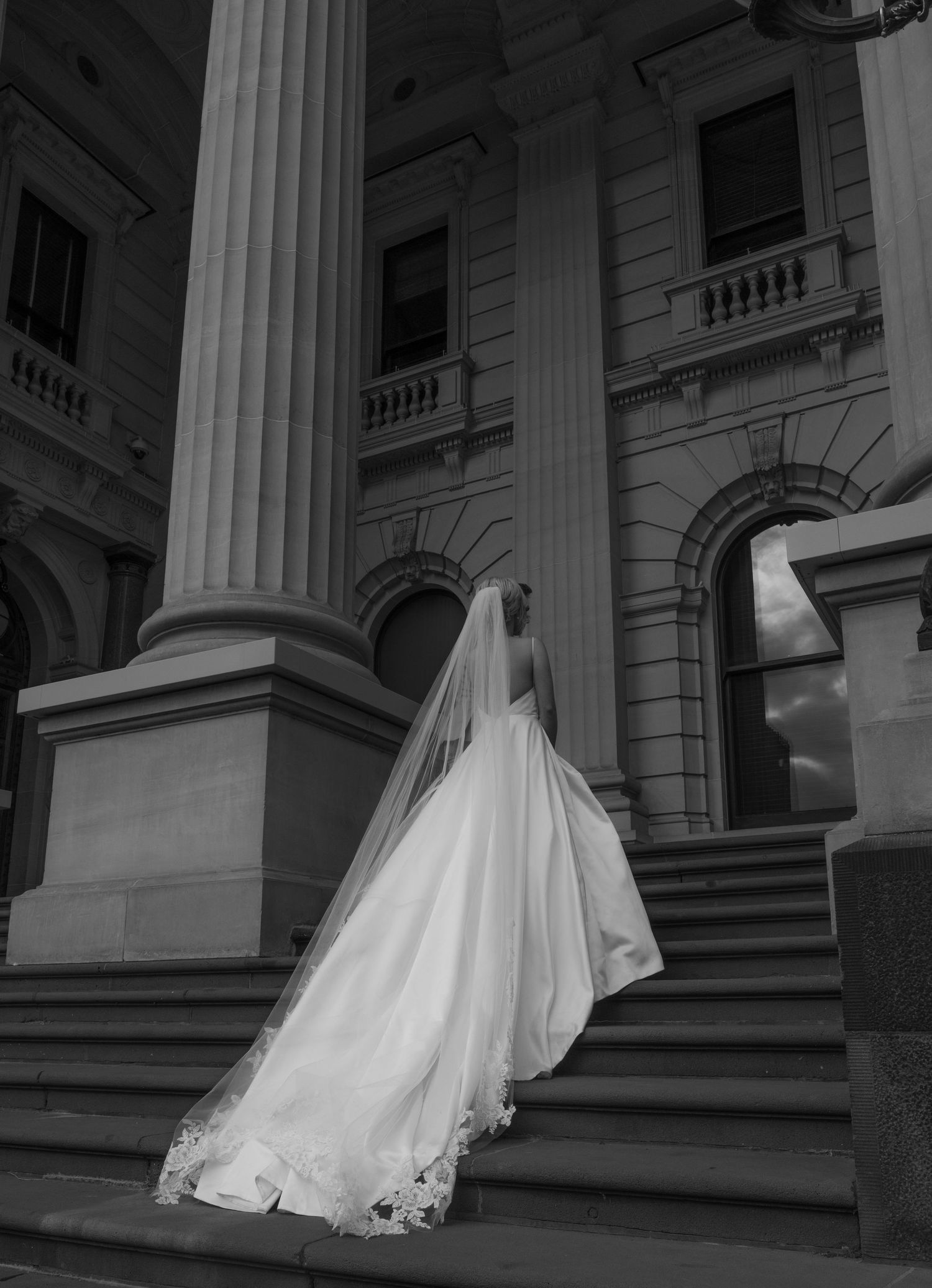 A series of black and white photographs showing a flowing white wedding dress in motion against a classical building facade.