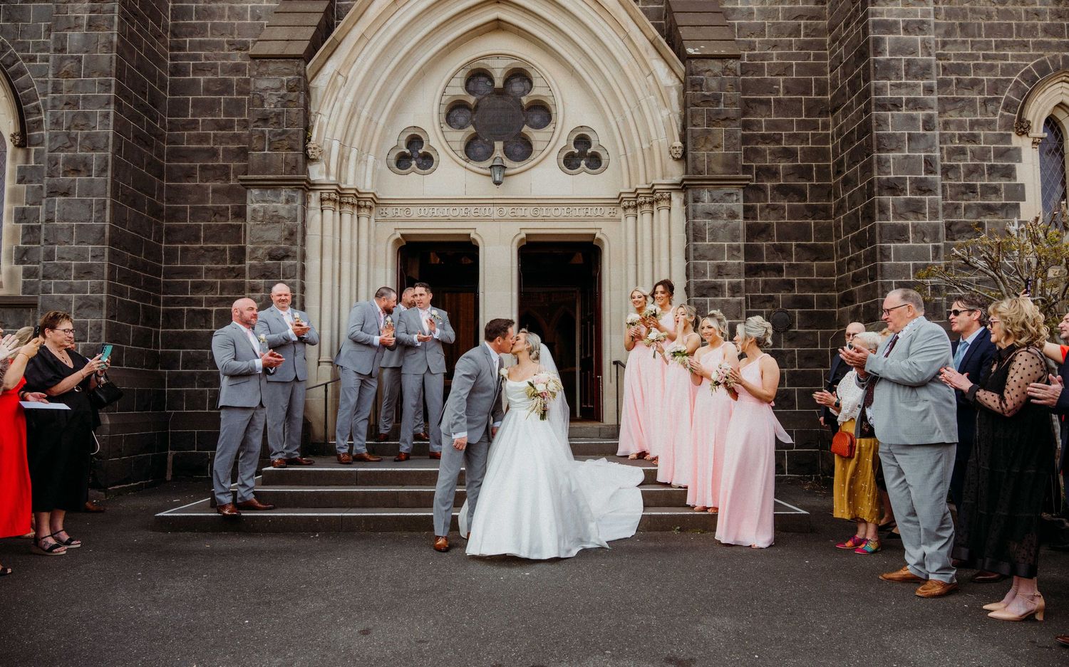 Wedding party celebrates during outdoor reception by historic brick church building with gothic architecture details.