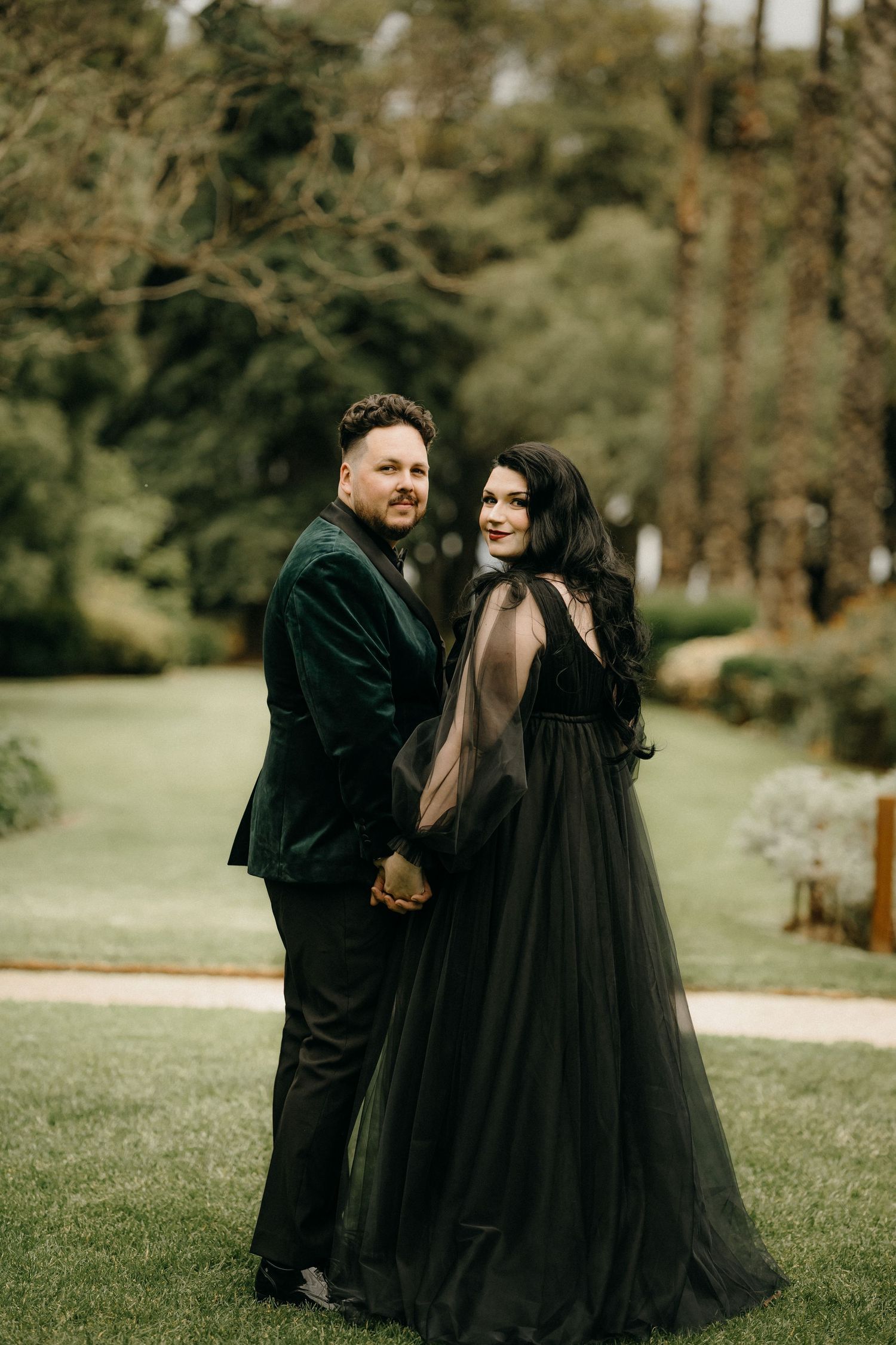 A couple in matching black outfits share romantic moments in a wooded outdoor setting.