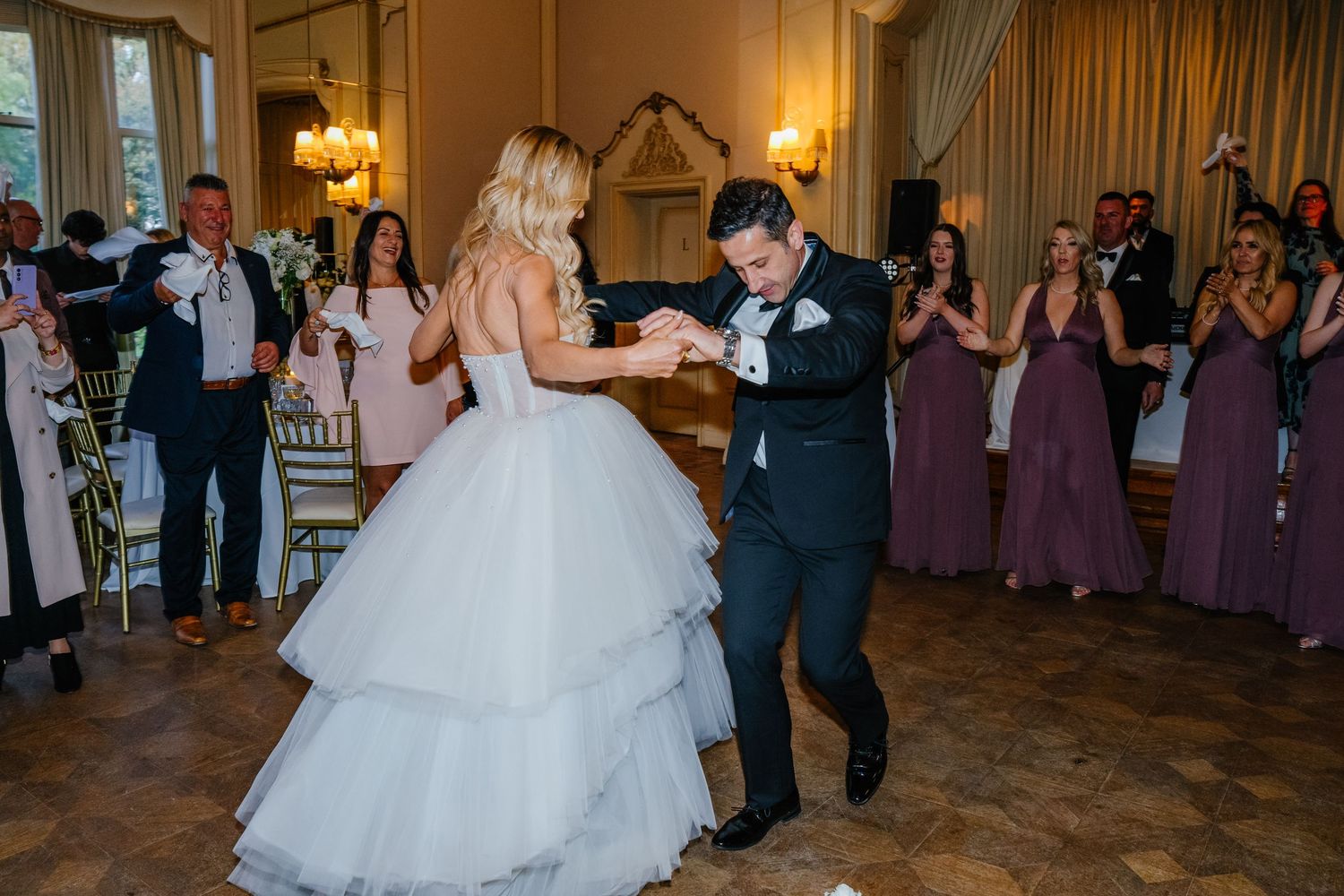 A couple shares their first dance at an elegant wedding reception while guests watch from the sides.