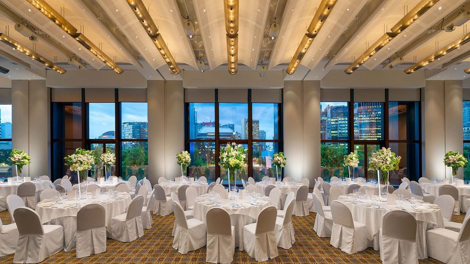 Elegant ballroom setup with white chair covers and panoramic windows overlooking a scenic waterfront view.