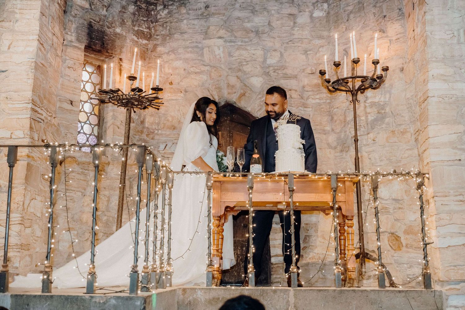 A wedding ceremony takes place at an elegant stone venue with rustic candelabras and a wooden table for signing documents.