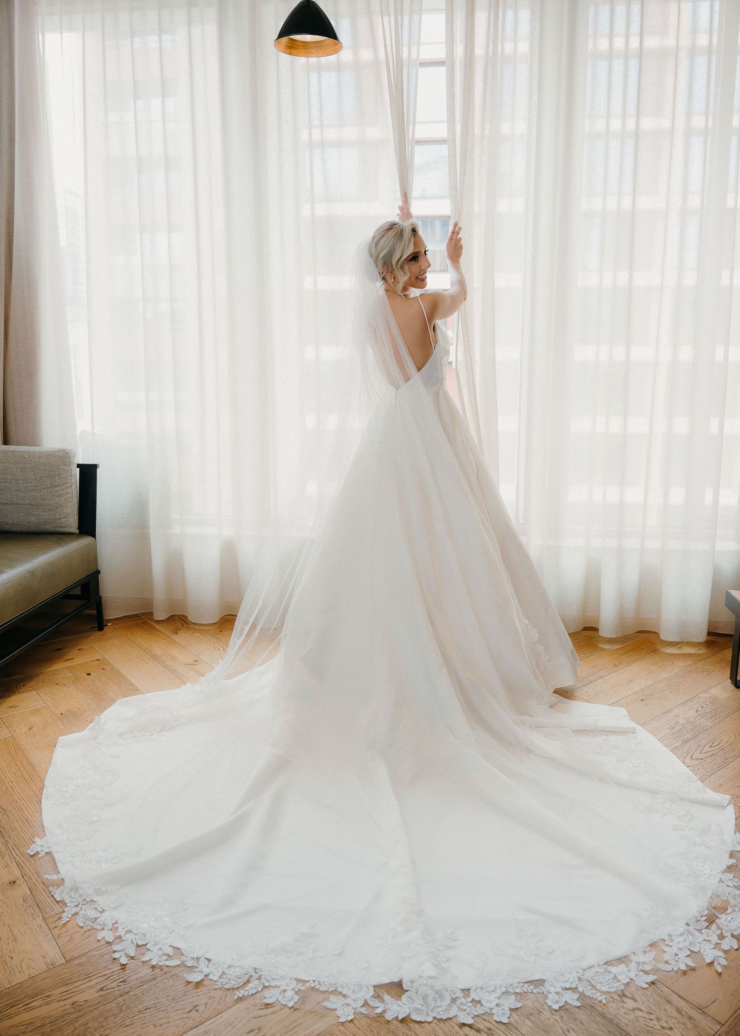 A stunning white wedding dress with a cathedral-length train and delicate lace details displayed in a bright room.
