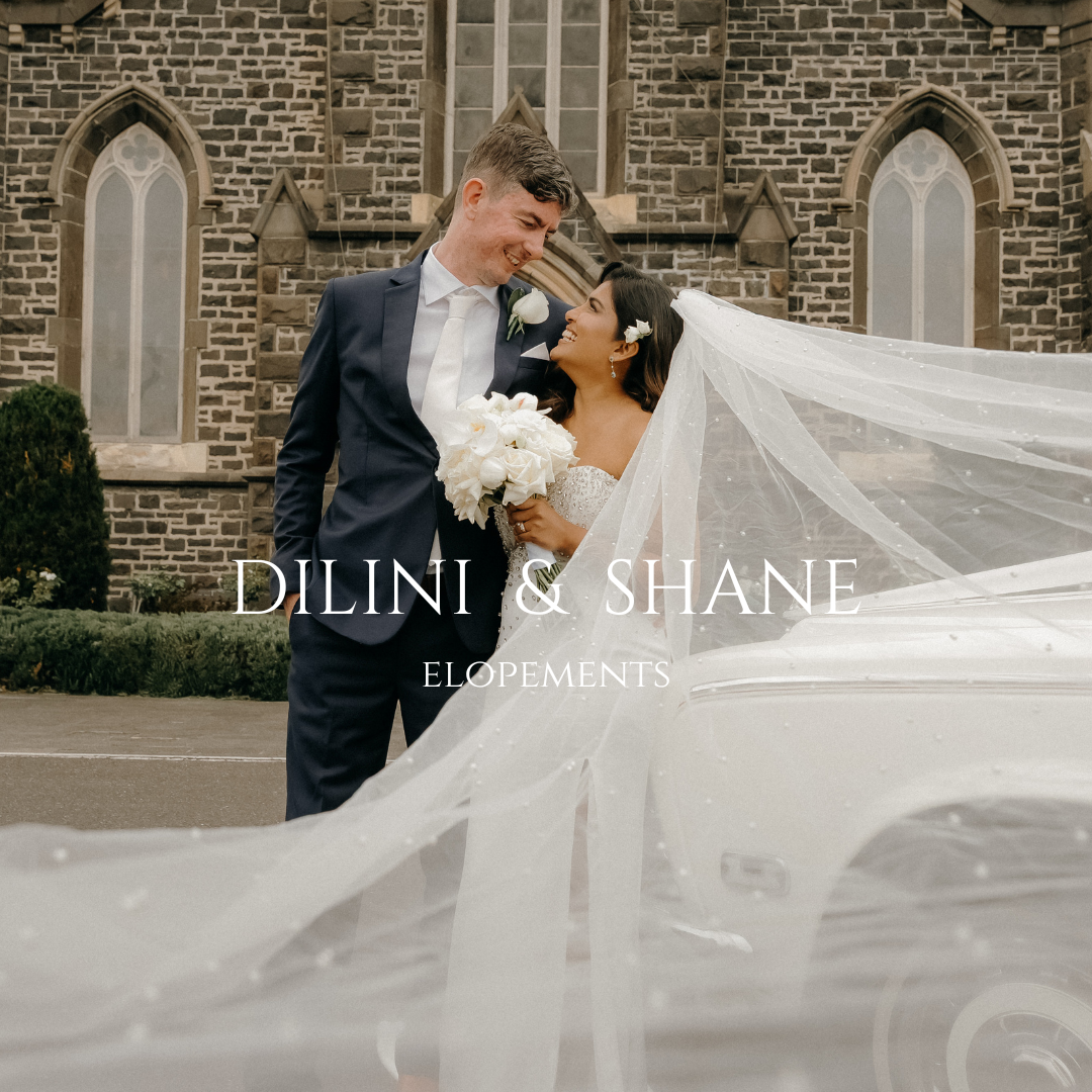 A bride and groom share an intimate moment outside a stone church as her long veil flows dramatically in the wind.