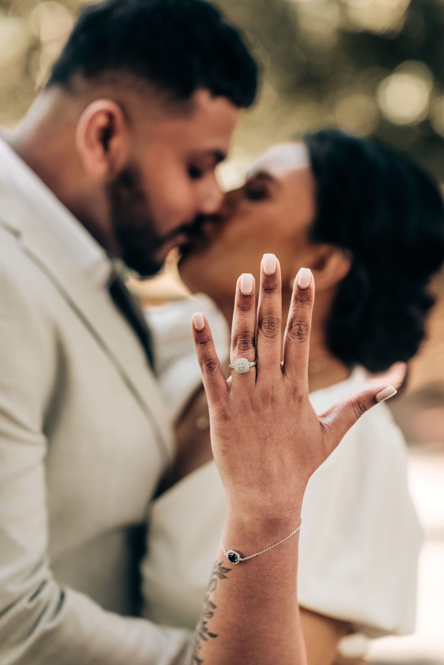 Close-up photo showing wedding bands and engagement rings on hands against a soft blurred background during a ceremony.