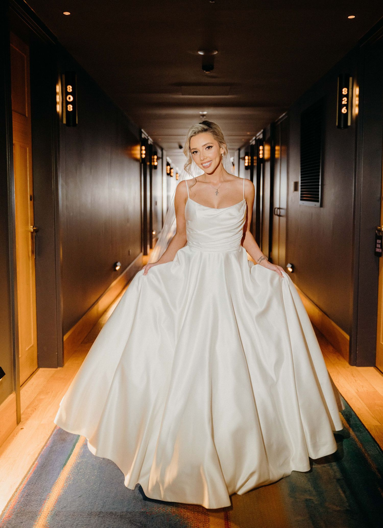 A bride in a flowing white ballgown twirls gracefully in a dimly lit hotel hallway.