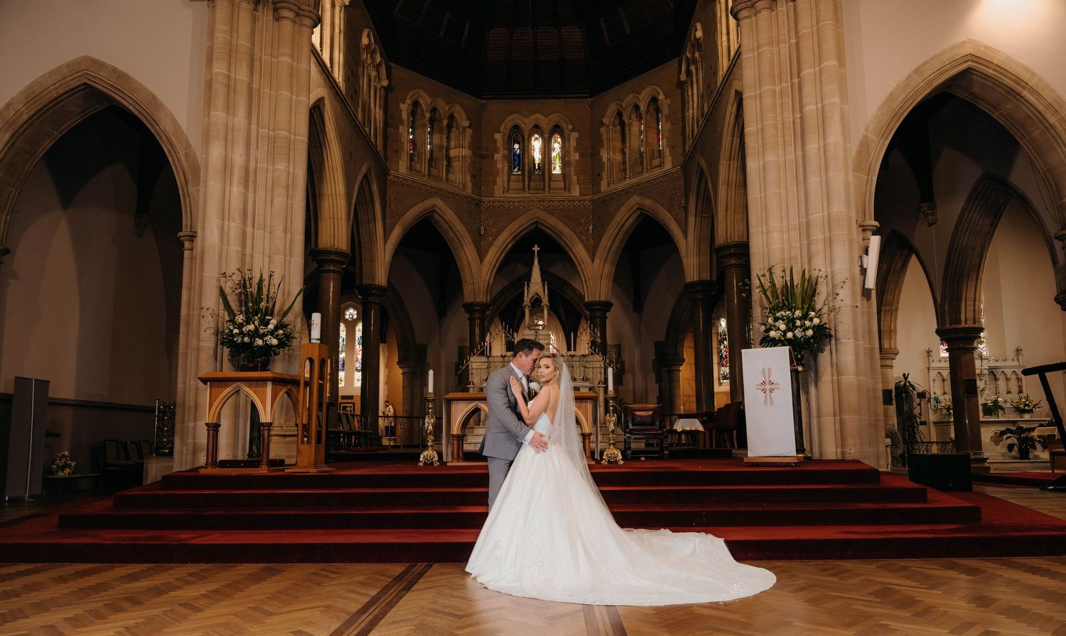 A panoramic view of a grand cathedral interior with Gothic arches and a bride in a white gown standing in the center.
