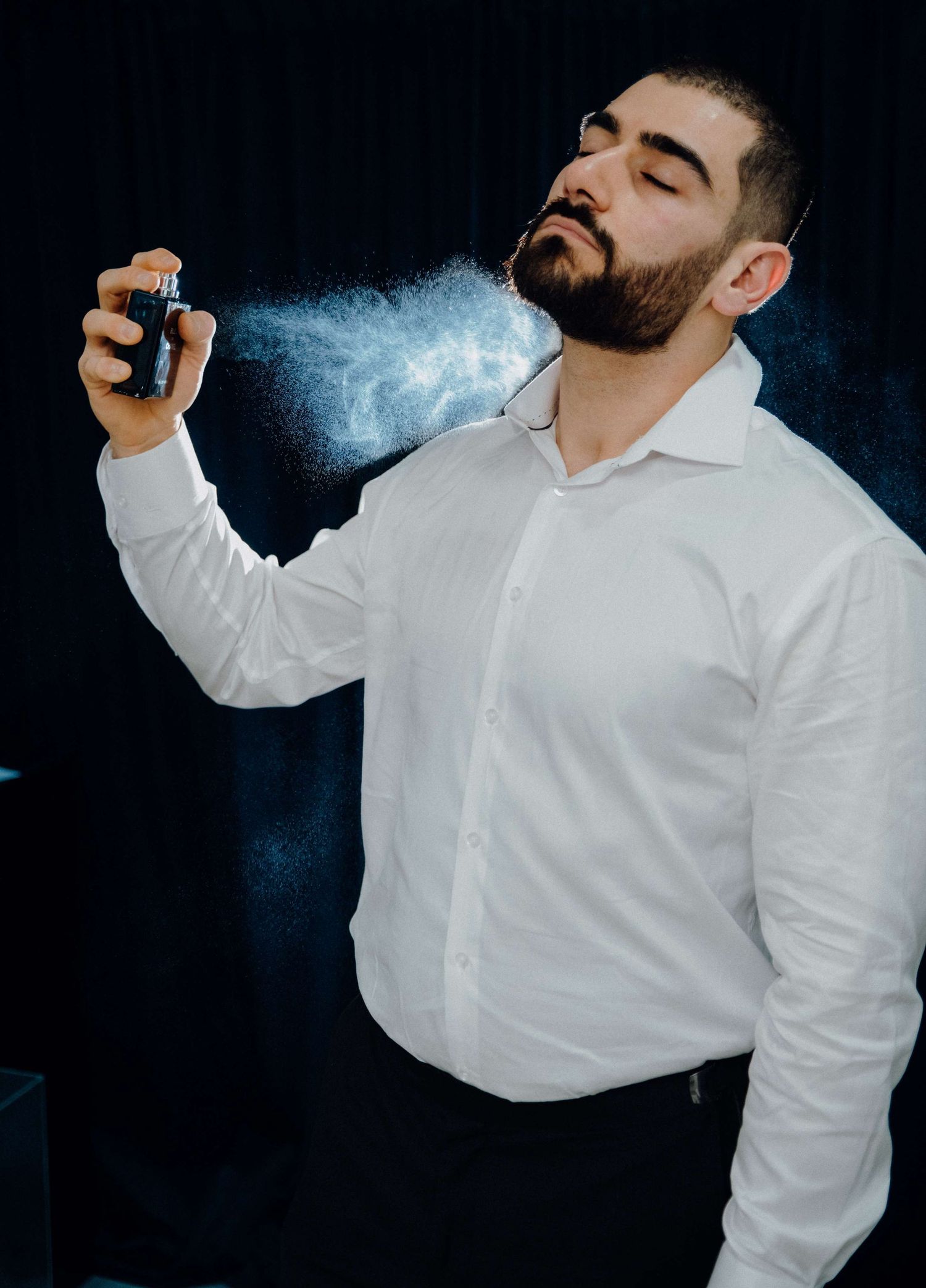 Multiple shots of person spraying cologne or perfume while wearing crisp white button-down shirt.