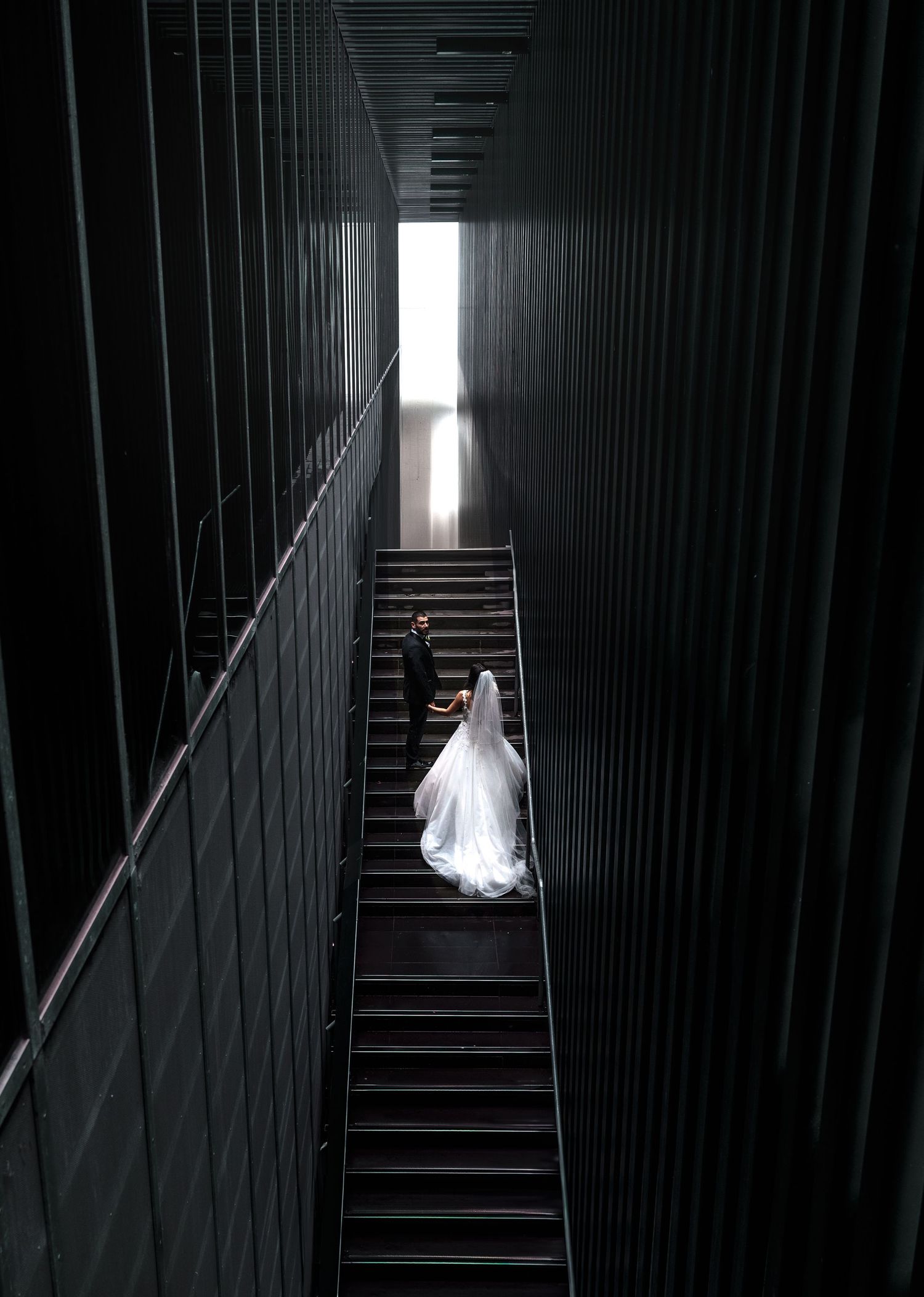 A bride in white dress ascends dark stairs, creating a dramatic contrast in a narrow corridor with multiple perspectives.