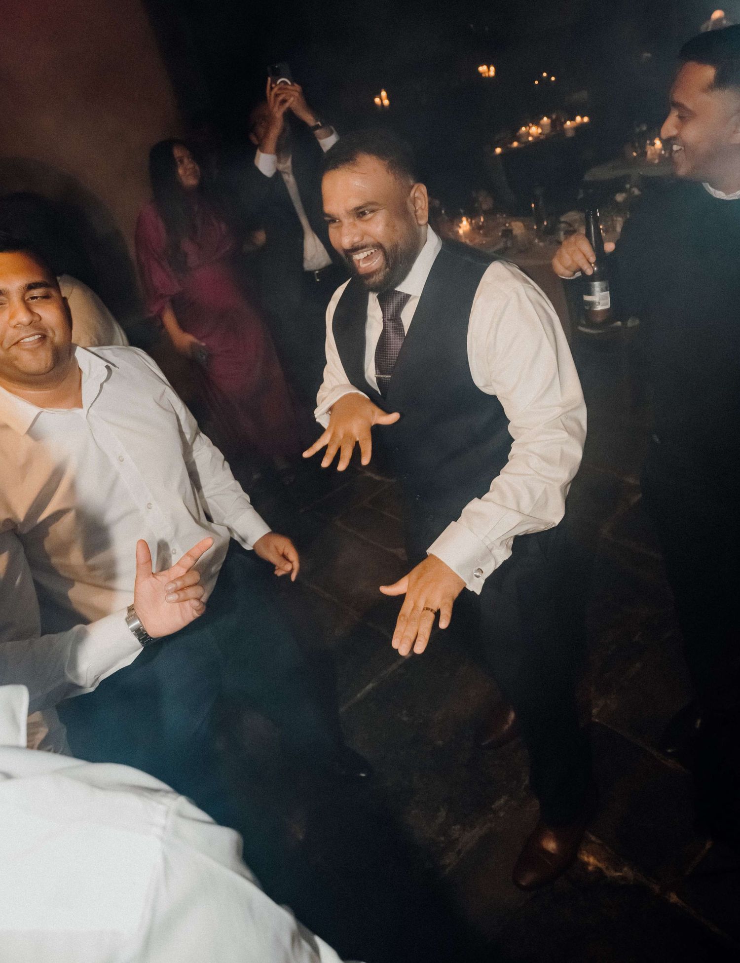 People dancing and celebrating at a wedding reception with atmospheric lighting and energetic movements.