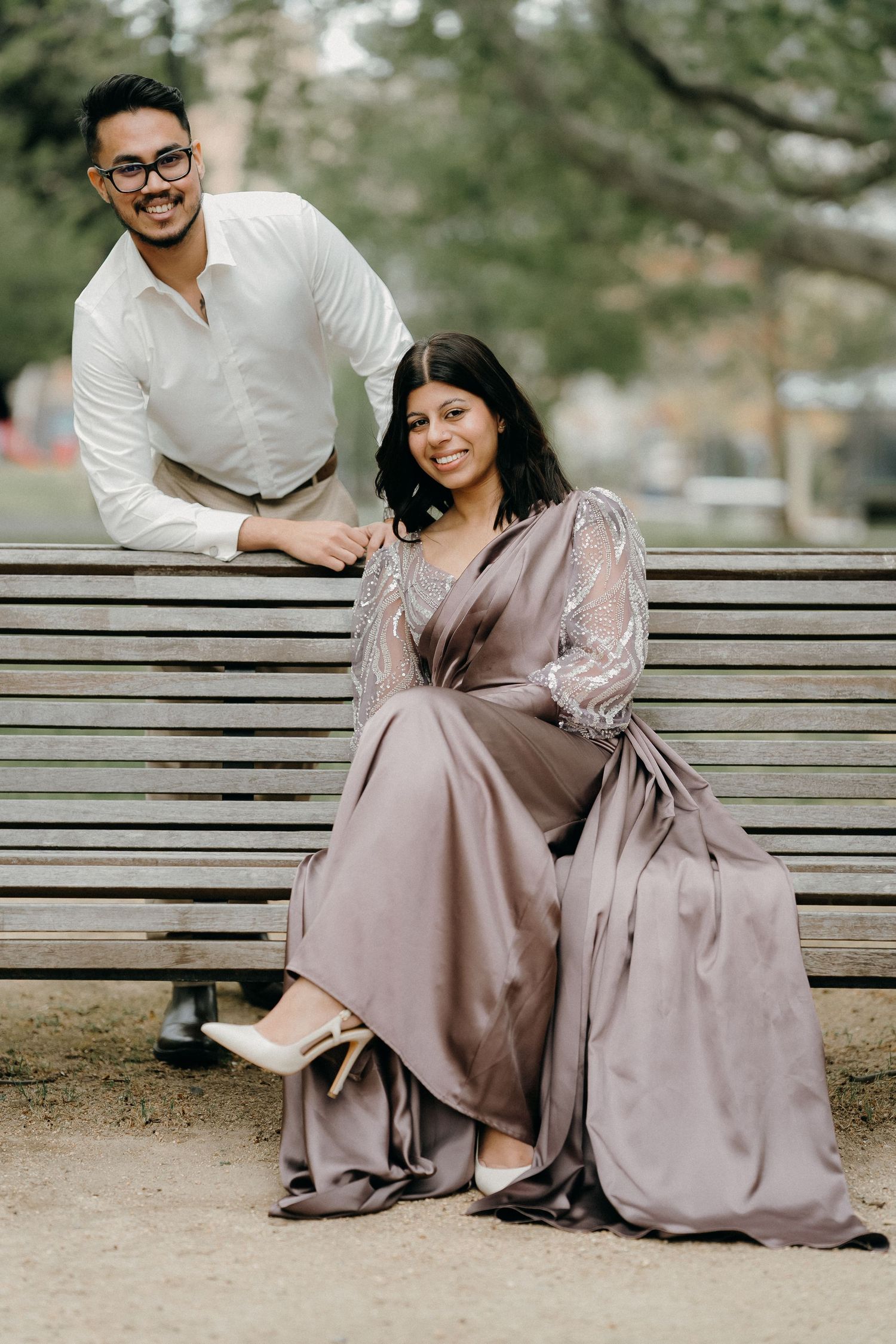 A couple in coordinated formal attire sits together on a wooden park bench sharing intimate moments.