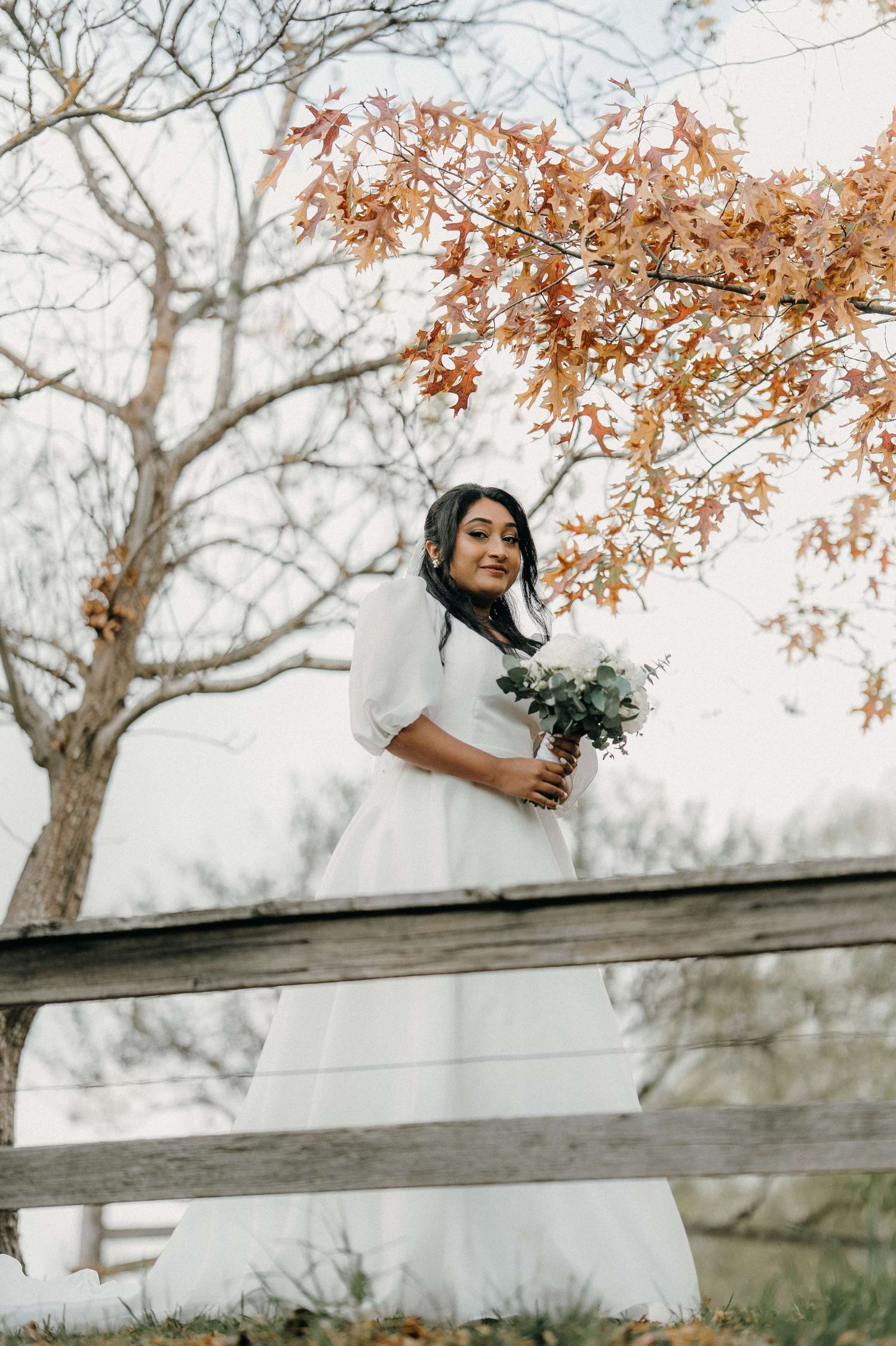 A romantic moment between newlyweds in white wedding attire against autumn foliage and foggy trees.
