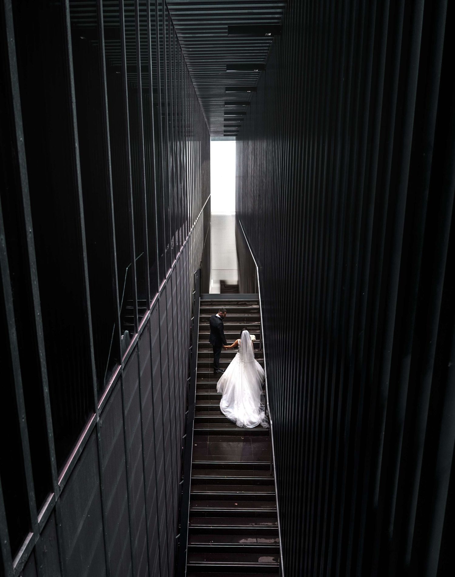 A person in a flowing white gown descends dark industrial stairs in a dramatic architectural space.