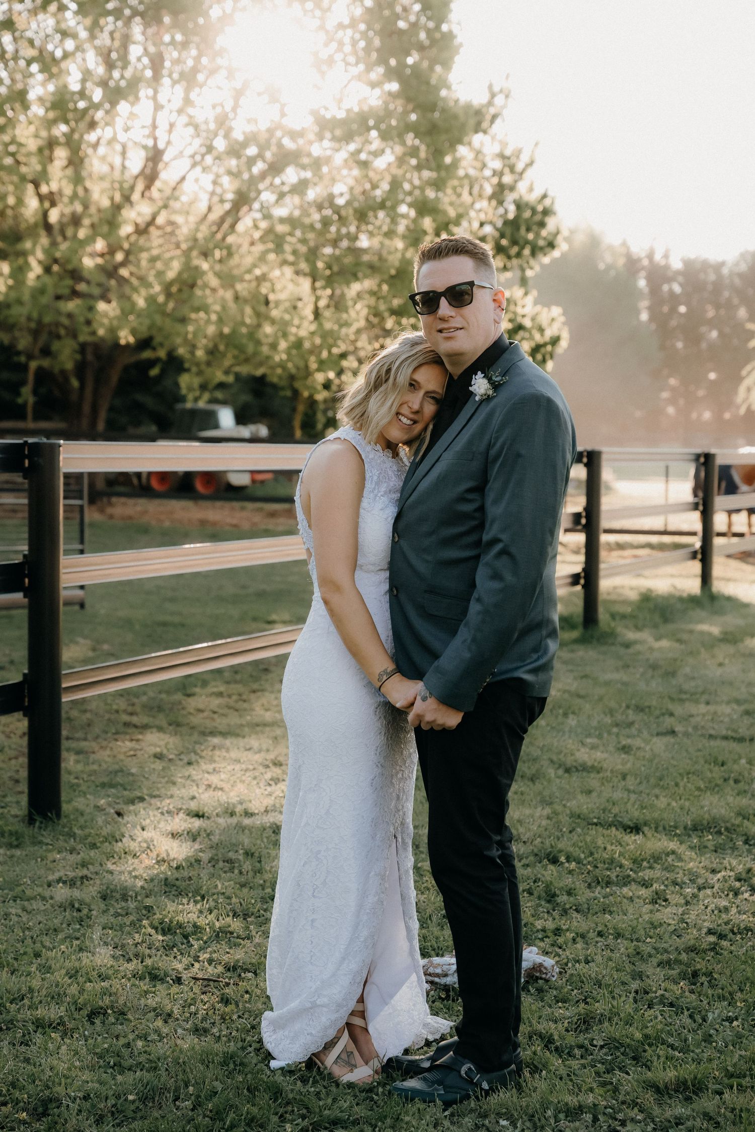A couple shares an intimate moment in a sunlit field with wooden fence posts in the background during a photoshoot.