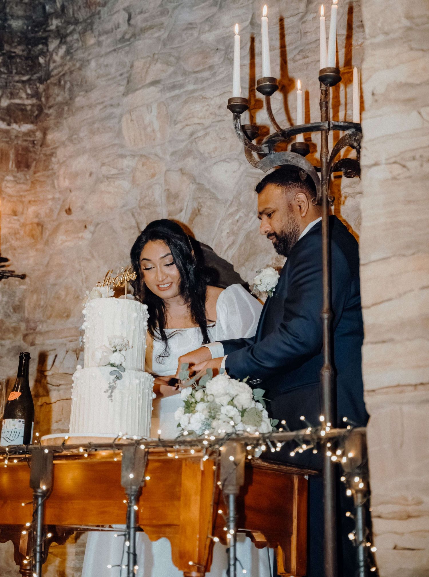Newlyweds sharing a romantic moment while cutting their elegant white wedding cake at an intimate reception venue.