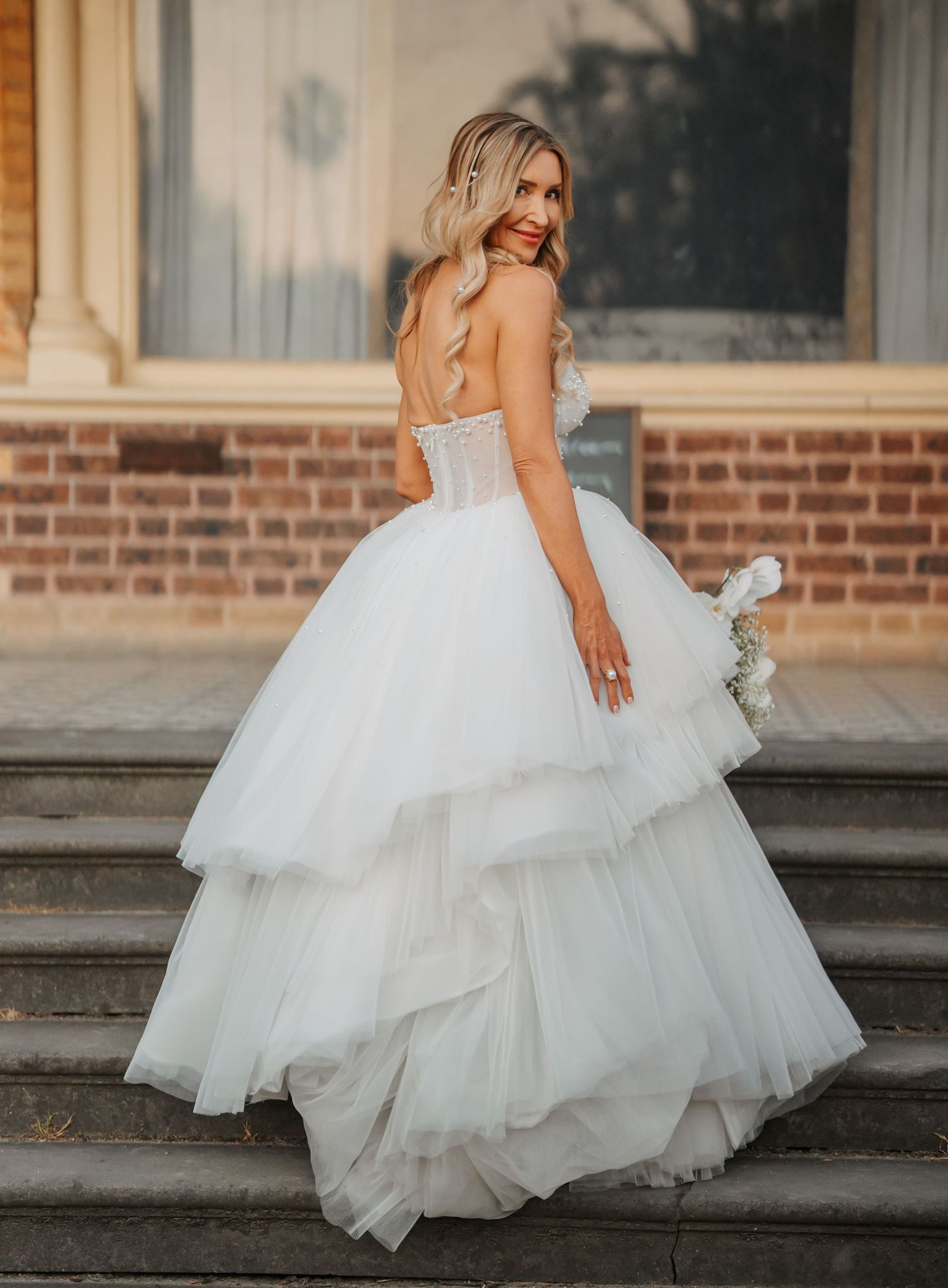 A stunning white layered tulle wedding gown with corset bodice and tiered skirt photographed on brick building steps.