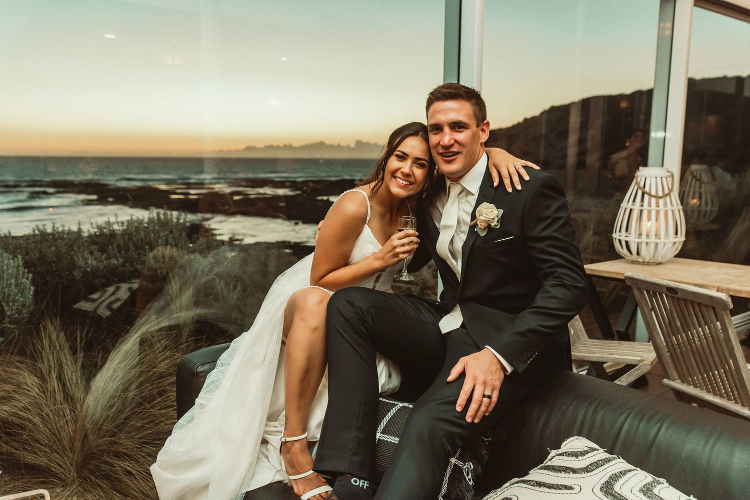 A romantic couple shares intimate moments together on an outdoor patio sofa during a sunset photoshoot.