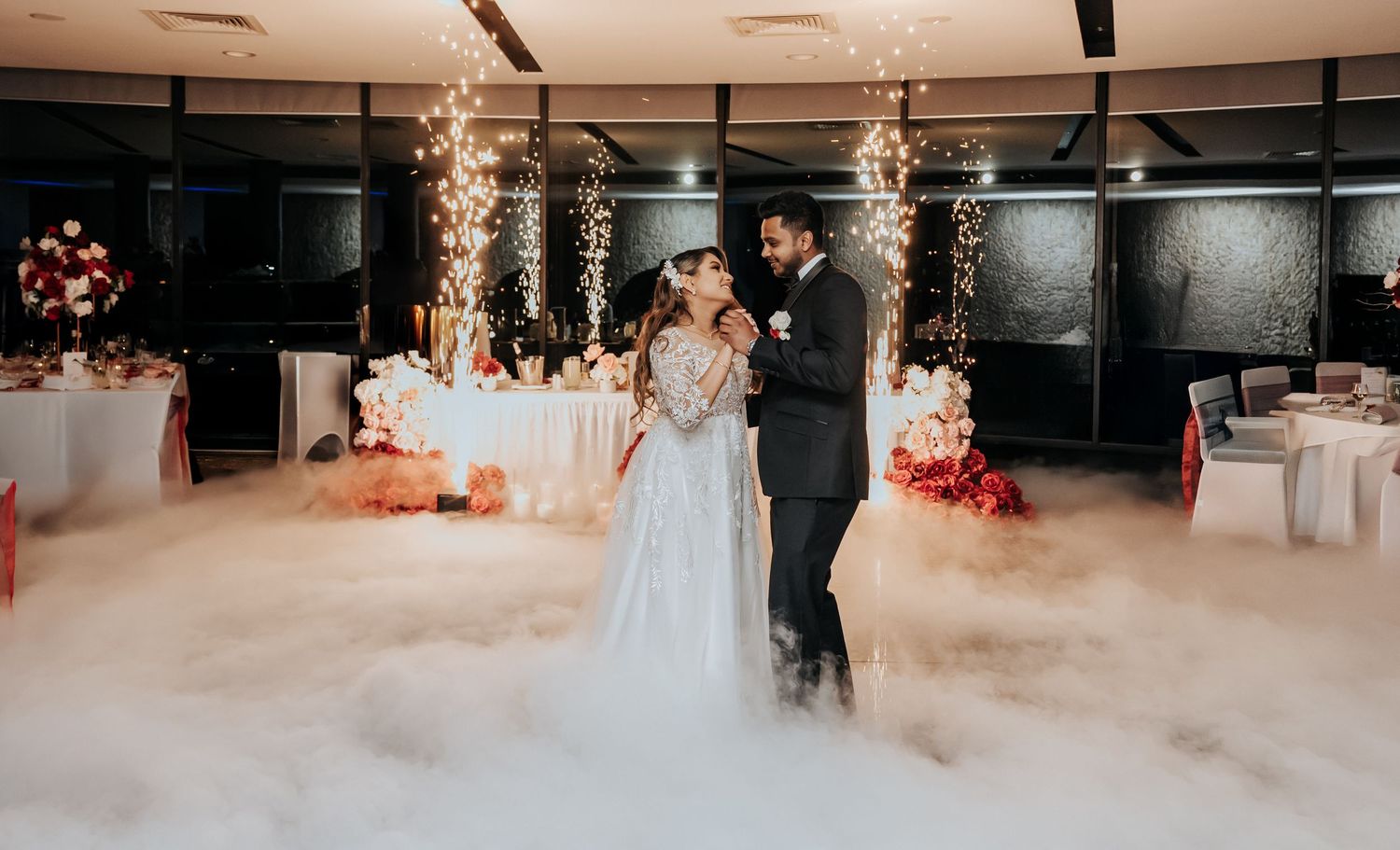 A wedding reception venue with low fog effects and elegant chandeliers creates a dreamy atmosphere.