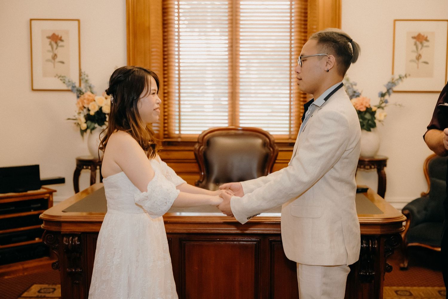 Two people in white wedding attire dance together during their first dance at an indoor reception venue.