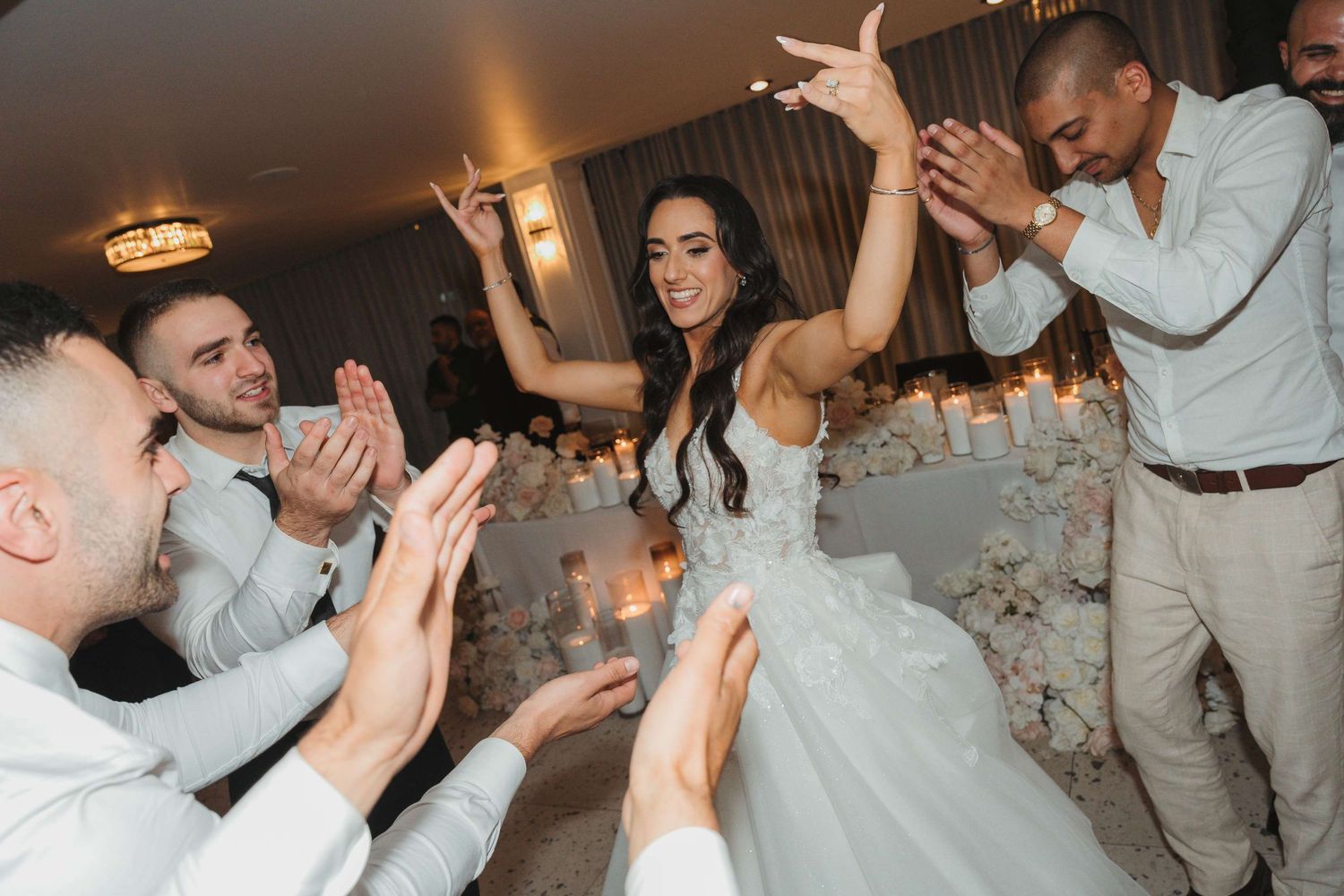 A group dances joyfully together at a wedding reception party in formal attire.