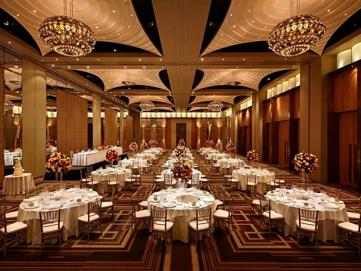 Elegant ballroom with crystal chandeliers and round dining tables set for a formal event with warm ambient lighting.