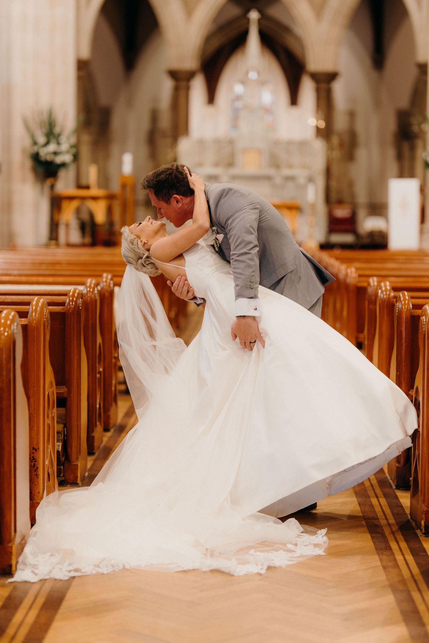 A romantic wedding couple shares intimate kisses while seated in wooden church pews during their special day.